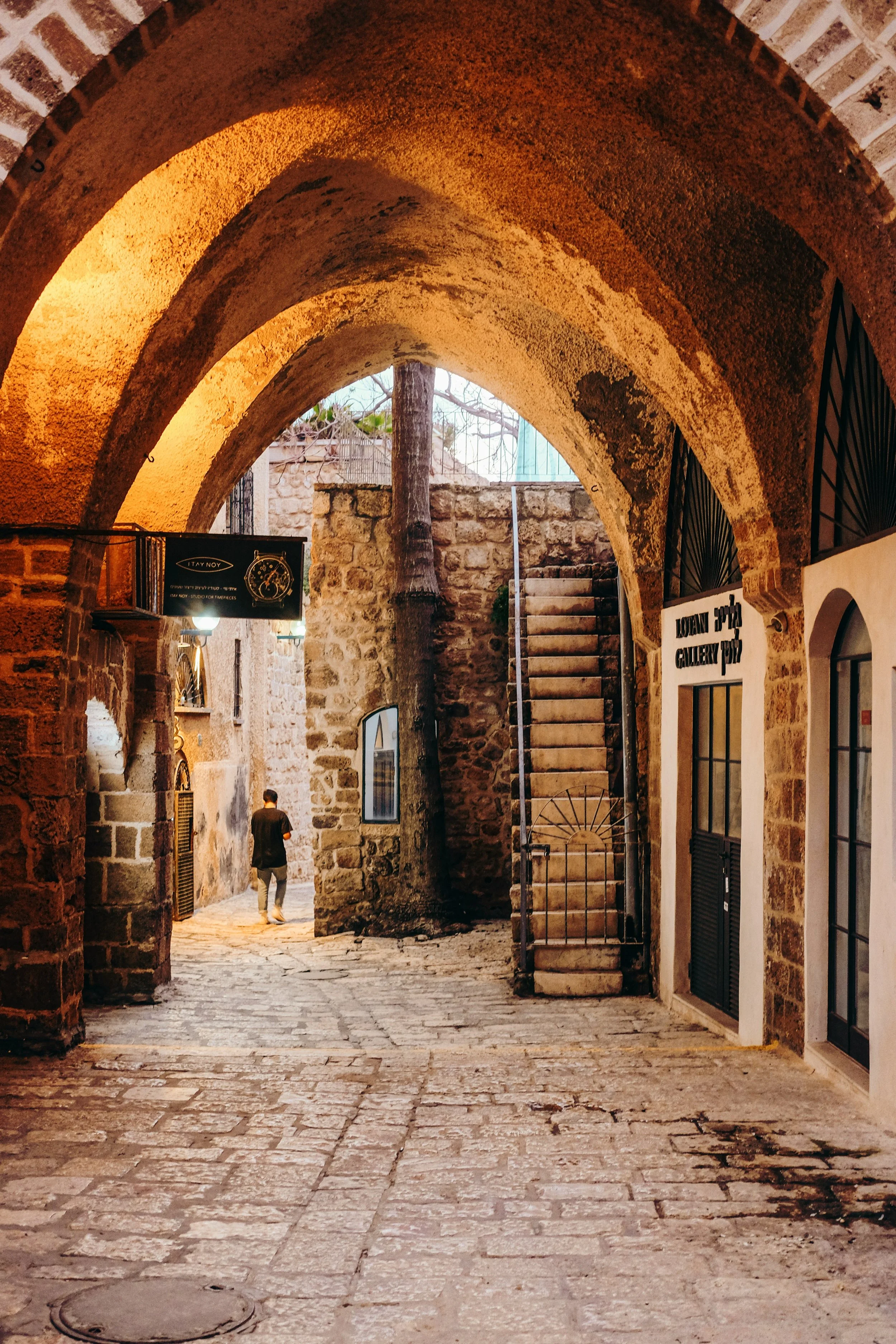 A lone figure walking down a cobblestone alleyway viewed through a stone archway in Jerusalem's Old City, on the Holyland Horizons After Dark tour
