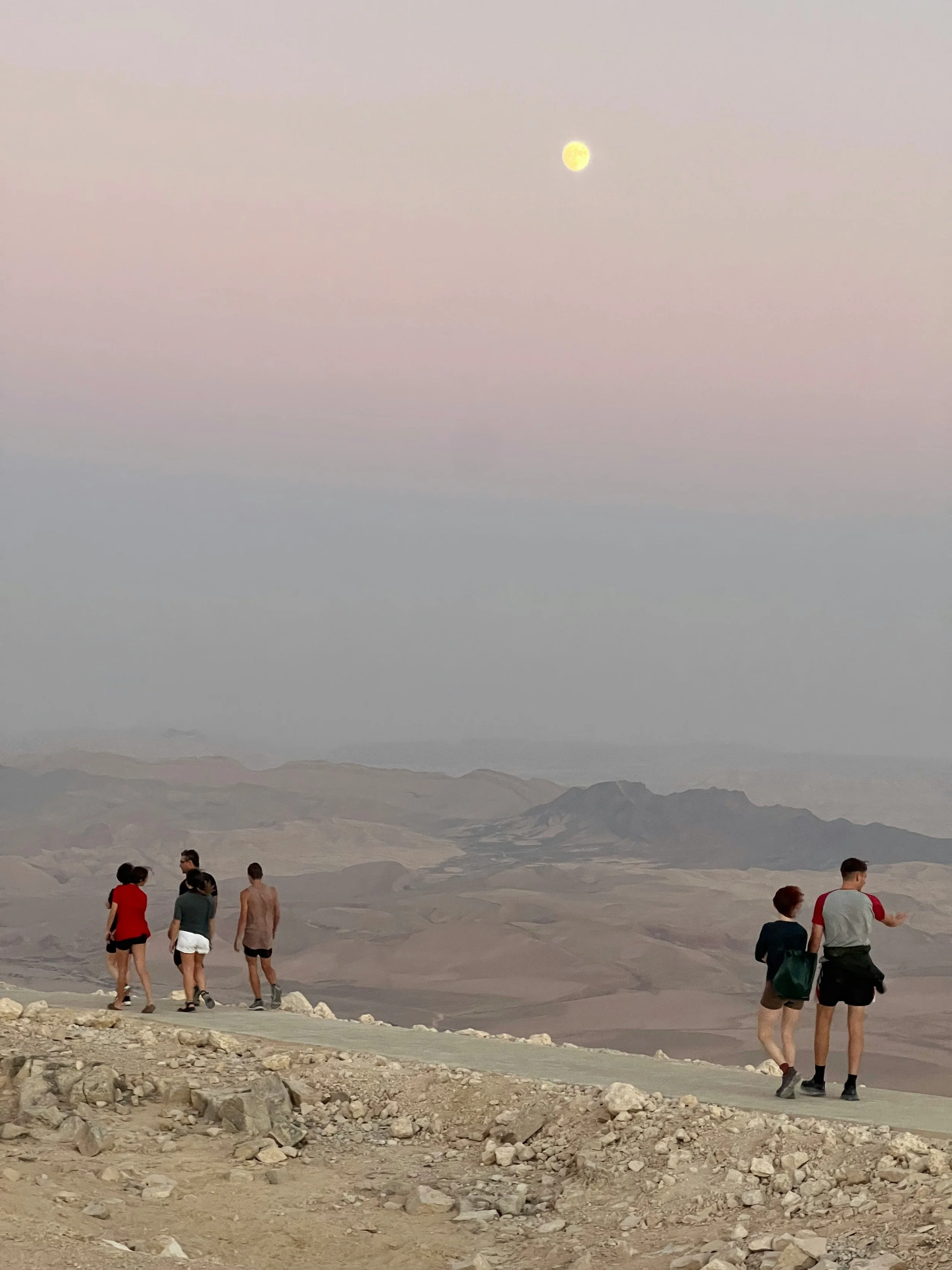 Group of travelers hiking on rocky desert terrain in the south of Israel at sunset with mountains in the background.