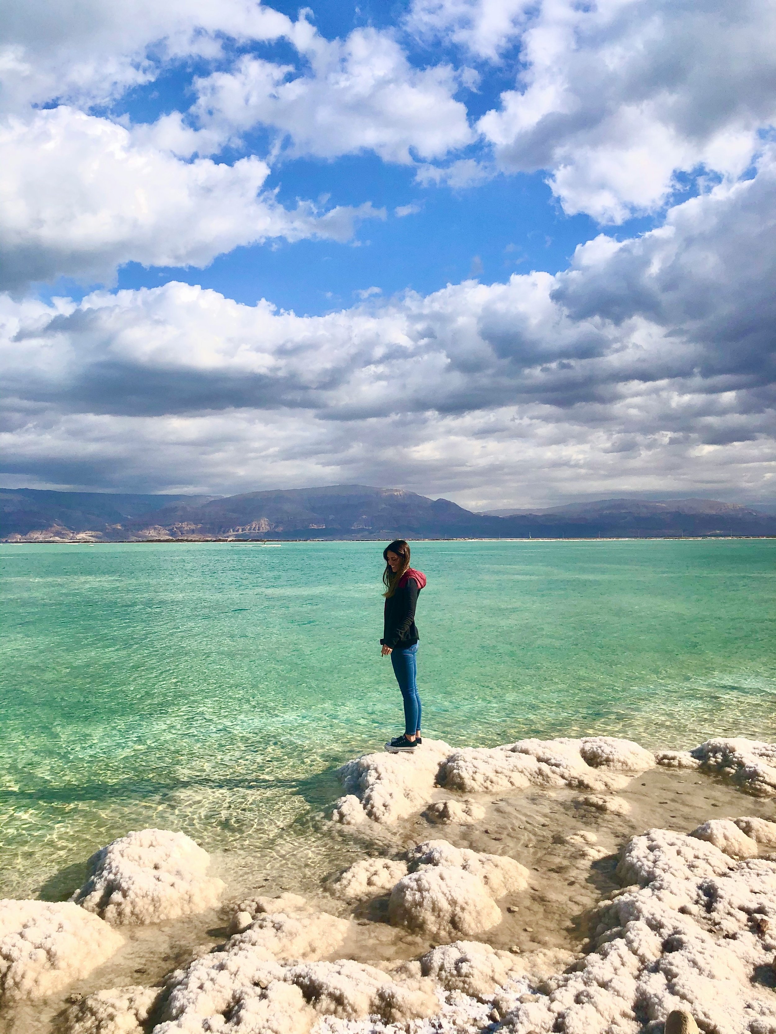 Woman standing on white salt flats at the Dead Sea, Israel, with distinctive salt formations covering the ground