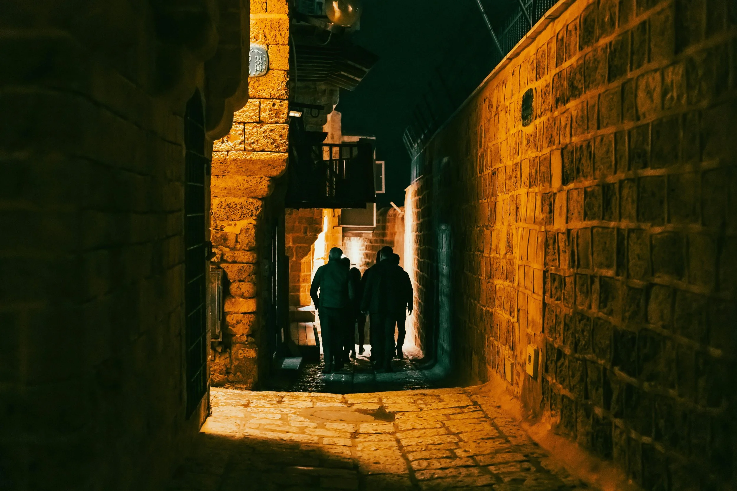 Visitors walking through a narrow dimly lit stone alleyway in Jerusalem's Old City at night, on the Holyland Horizons Jerusalem After Dark tour