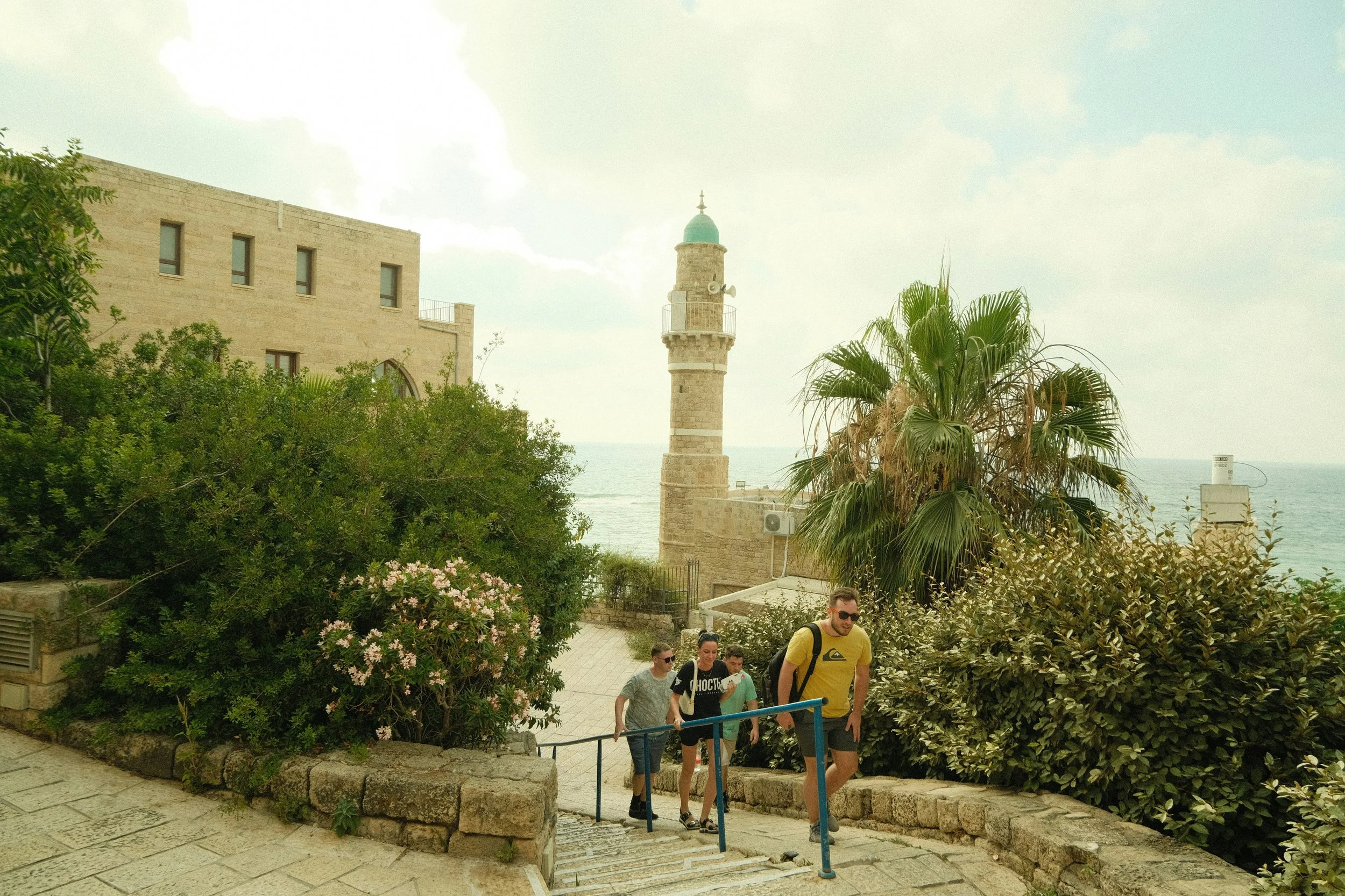 Tourists walking down stone steps surrounded by green bushes and flowers at a historic site in Israel.
