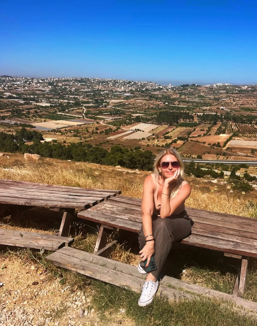Alena Levy, licensed Holy Land guide and co-founder of Holyland Horizons, sitting on a wooden bench with a scenic valley view in Israel