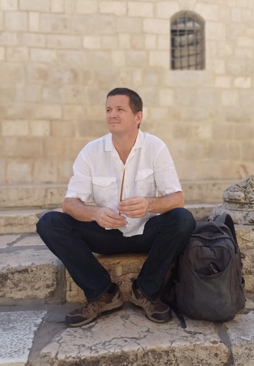 Toon Van Rompay, licensed Holy Land guide and co-founder of Holyland Horizons, sitting on stone steps outside a stone building in Israel