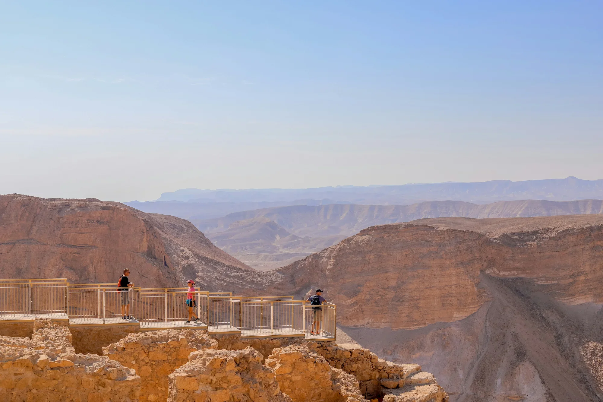Three travelers standing on a viewing platform overlooking a deep canyon with rocky cliffs in Israel, on a guided journey