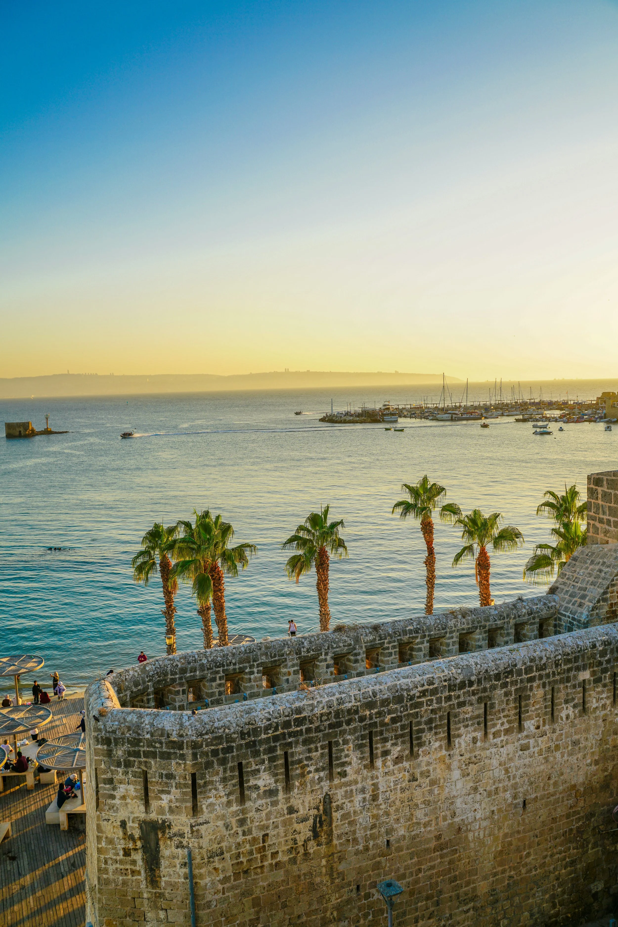 Historic stone fortress overlooking a marina with sailboats and palm trees in Caesarea, Israel, a destination on Holyland Horizons journeys