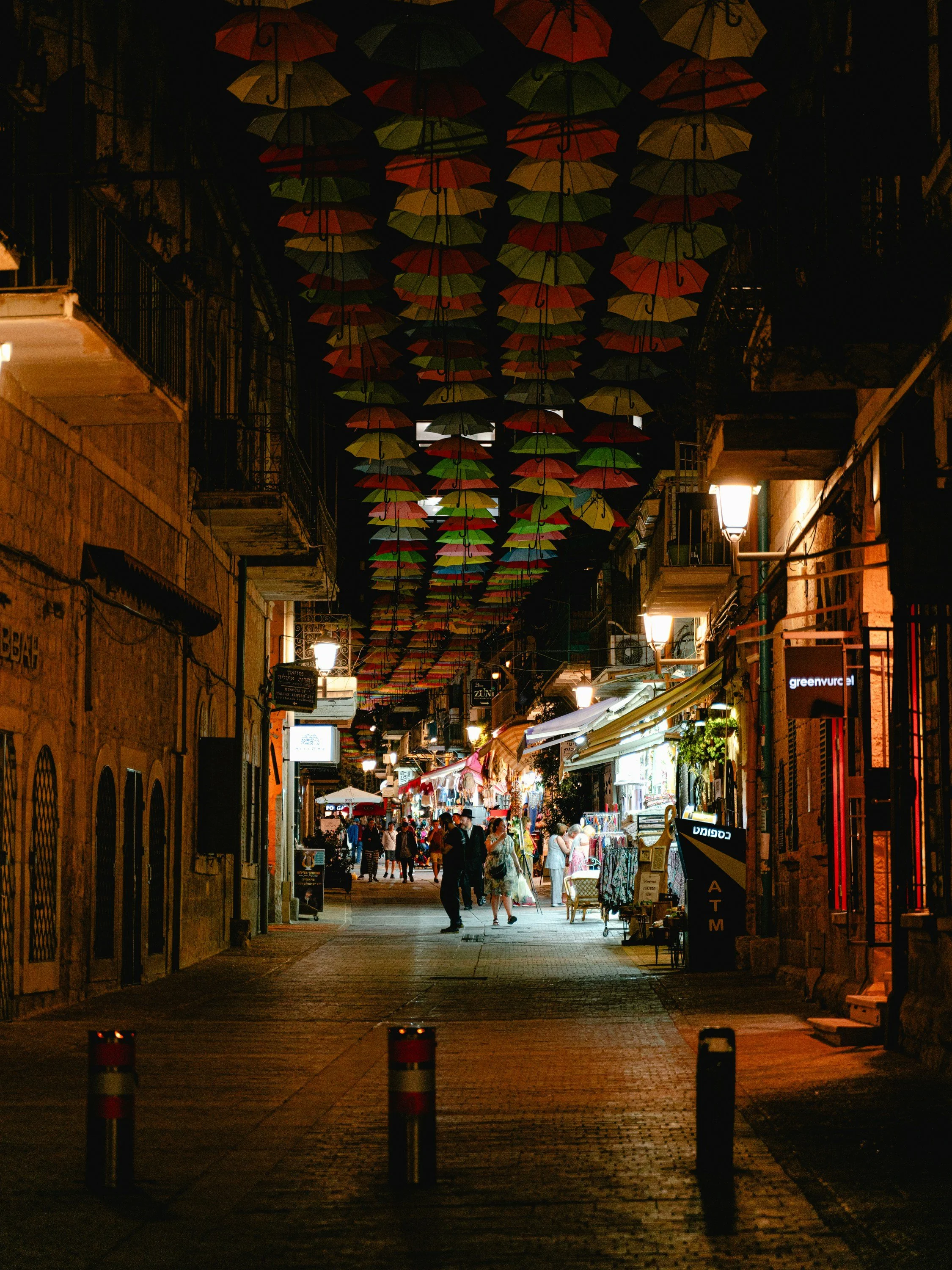 Colorful hanging umbrellas strung above a lively market street in Jerusalem at night, on a Holyland Horizons After Dark walking tour