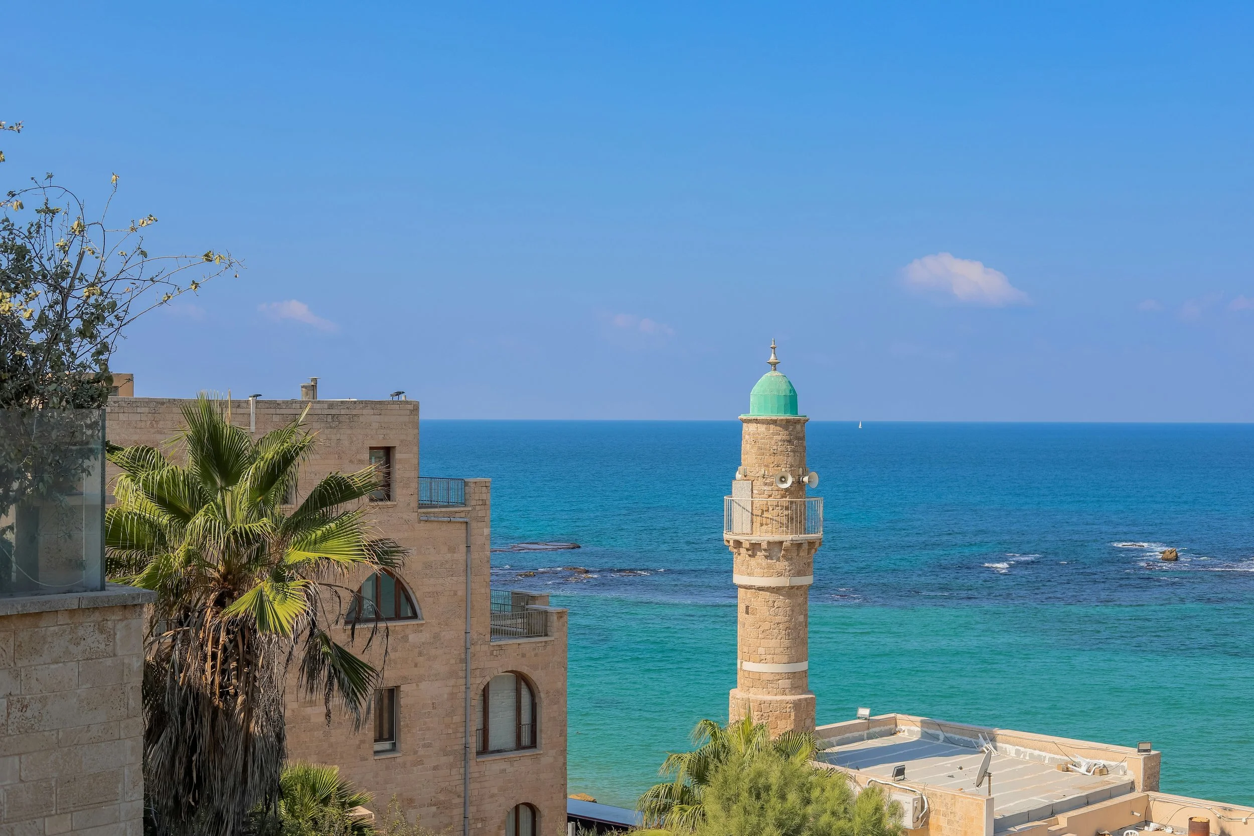 Coastal Mediterranean waterfront with a lighthouse and stone buildings in Israel, a landscape featured on Holyland Horizons journeys