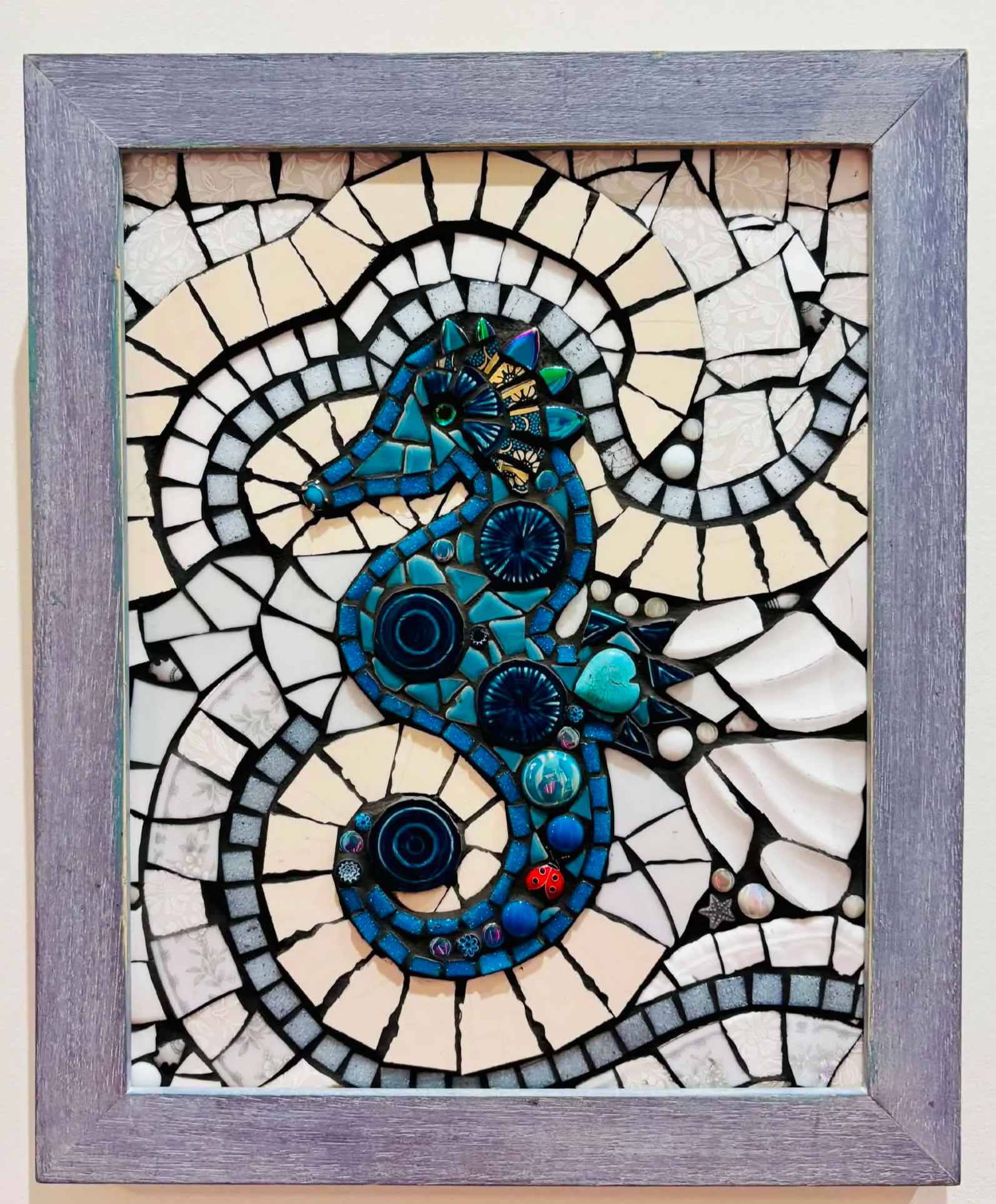 Mosaic art featuring a spiral design with blue, black, and white tiles, displayed in a wooden frame.