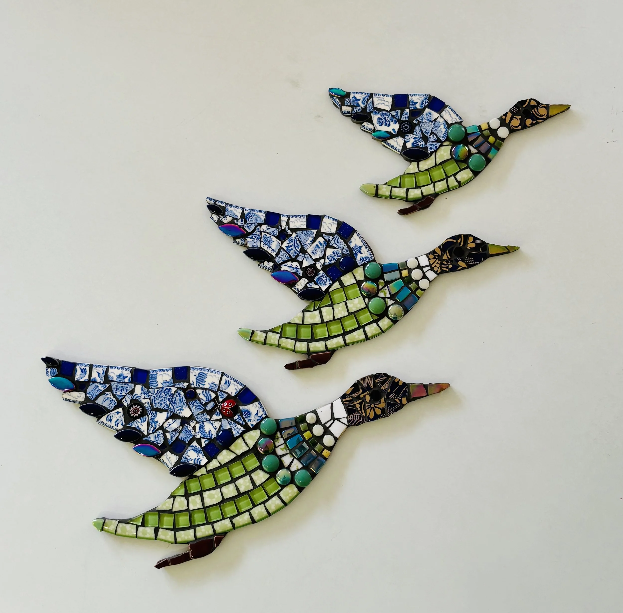 Colorful mosaic artist-made lizard sculpture with green and yellow body, blue and black tail, and intricate patterned details on a white background.