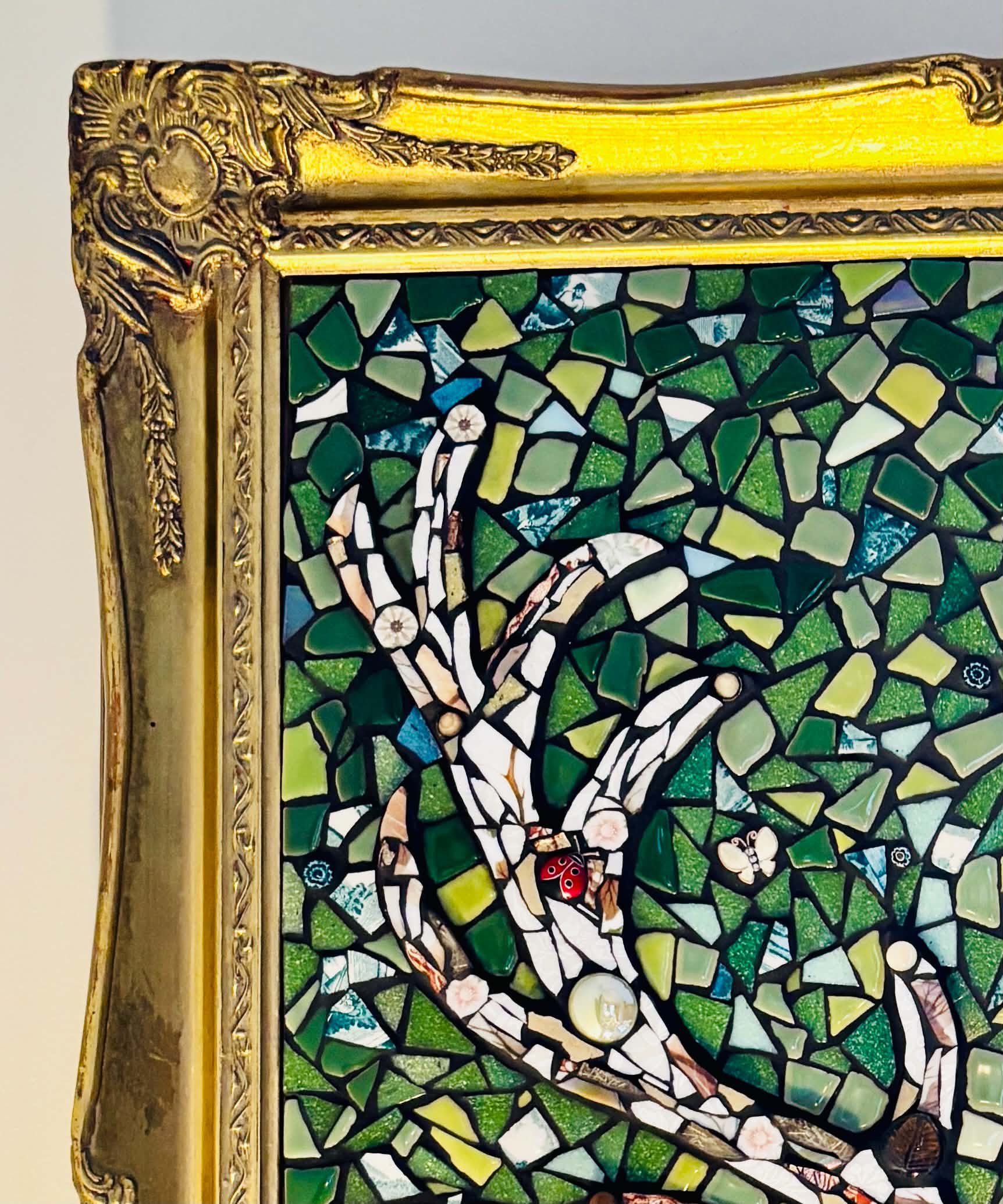 Close-up of a colorful mosaic artwork with various green, blue, and white pieces, surrounded by a decorative gold frame.