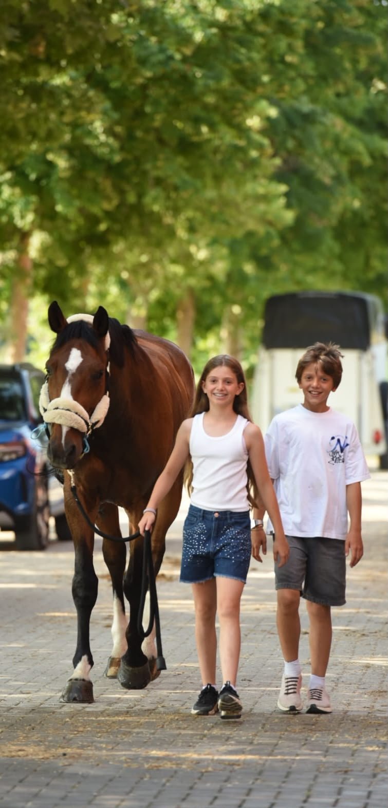 Due bambini, una ragazza e un ragazzo, che camminano con un cavallo in un parco alberato
