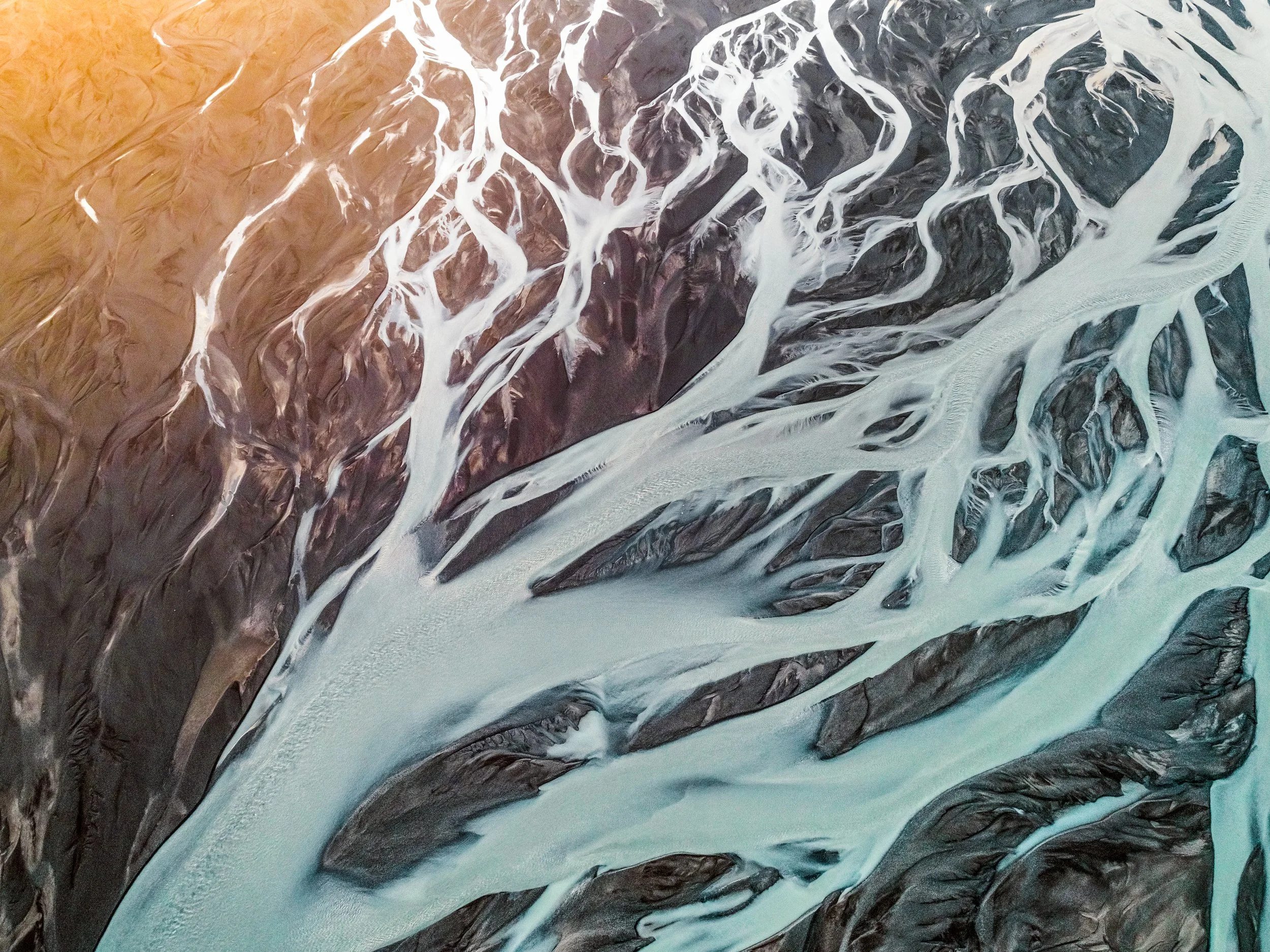 Aerial view of a river delta with braided waterways and sediment deposits, showing a mixture of orange, brown, black, and light blue water channels.