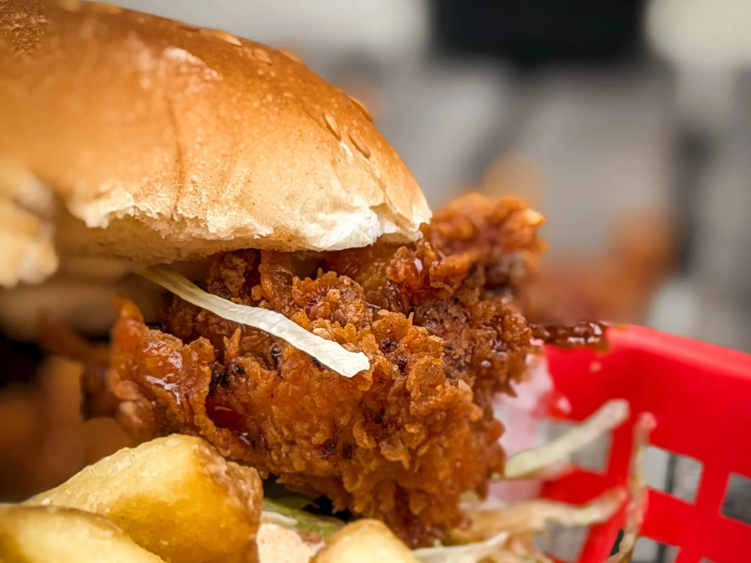 Close-up of a crispy fried chicken sandwich with a bun, fried chicken fillet, and some sauce.