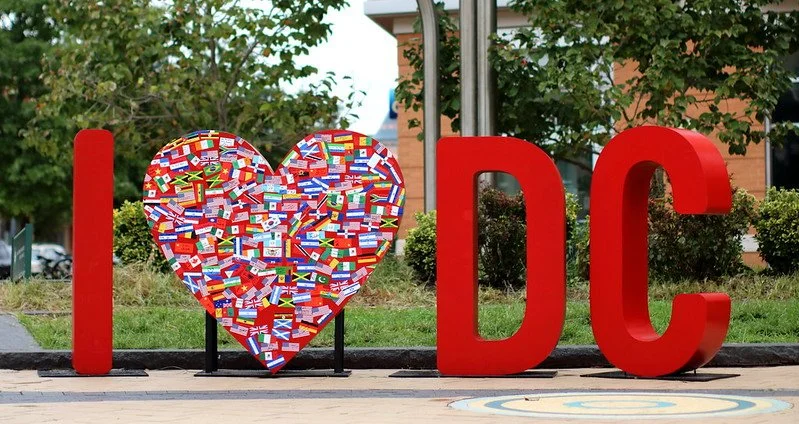 Large red letter 'I', a heart made of many small international flags, and large red letters 'DC' on a sidewalk.