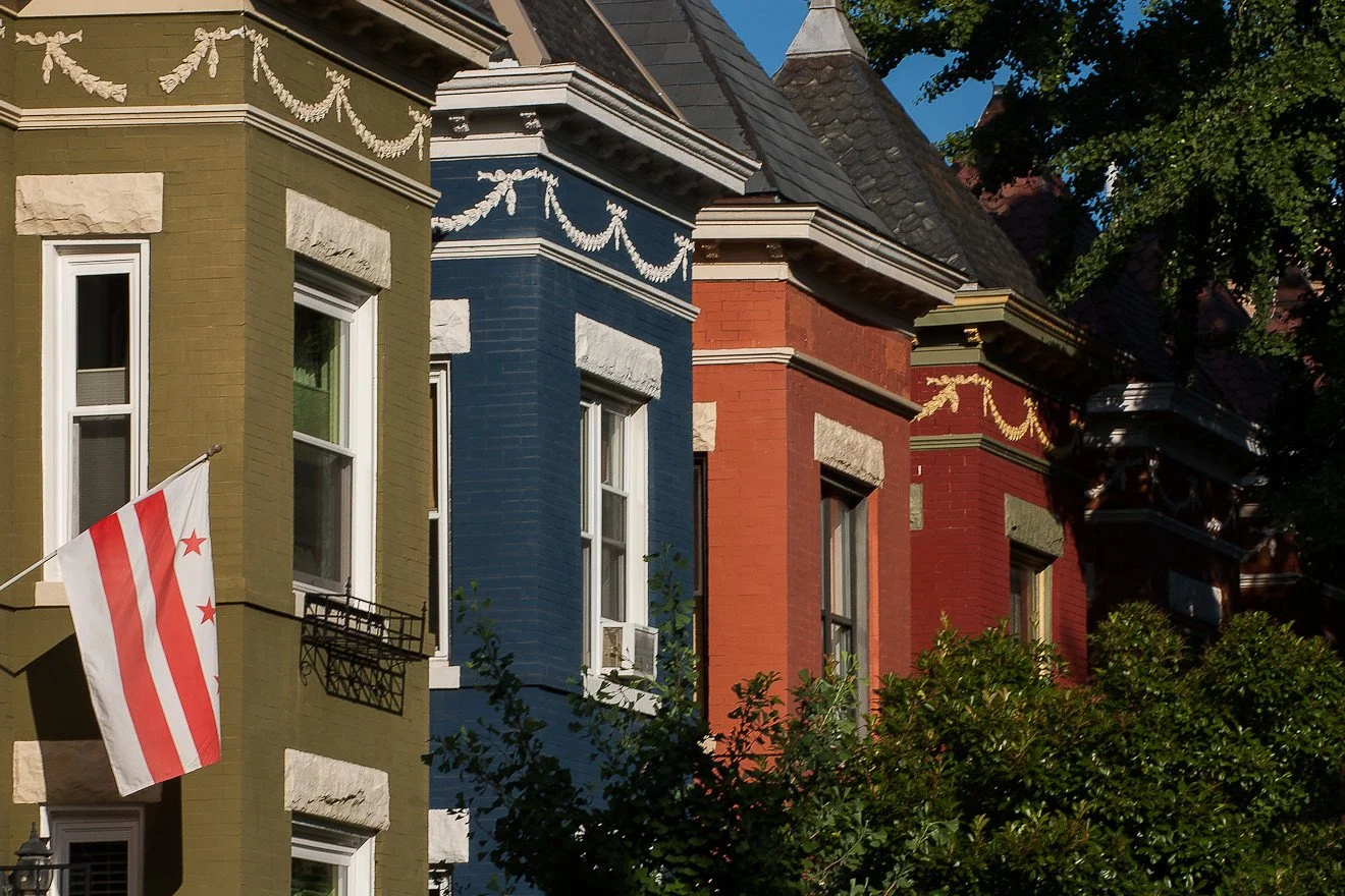Colorful row of Victorian-style houses in green, blue, and red with decorative trim and trees in the foreground.