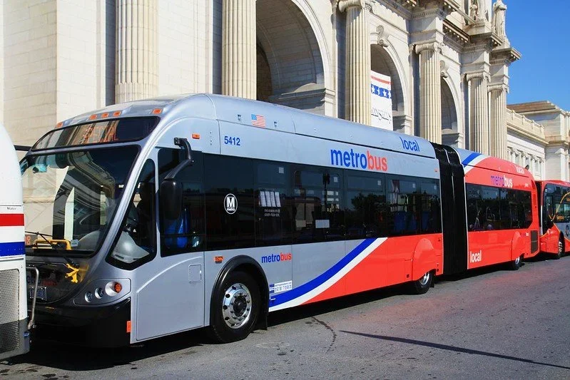 A modern double-decker metro bus parked on a city street near historic buildings.