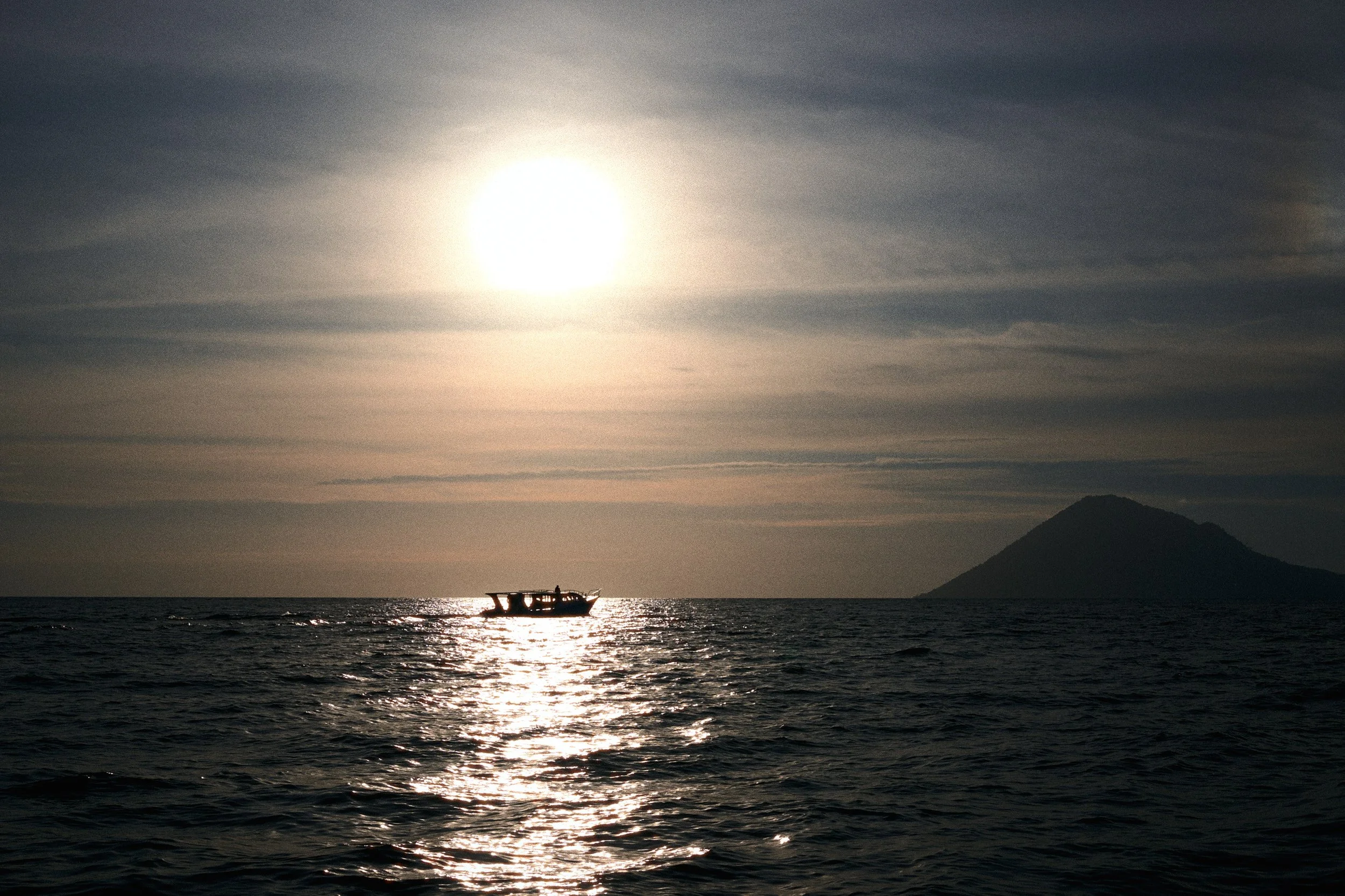 Photo of a boat on the water at sunset with a volcano (Manado Tua)  in the background