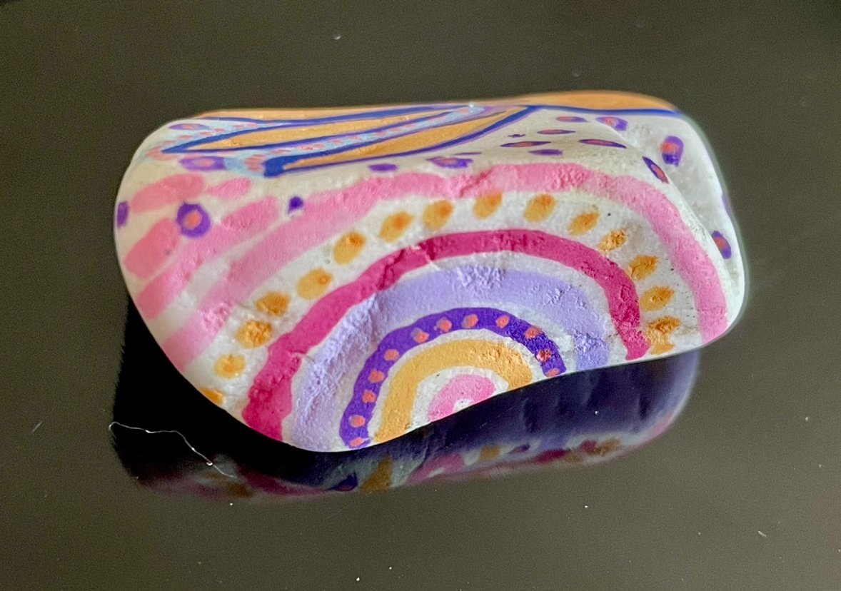Pierre peinte colorée avec des motifs de lignes en arc et points dans des teintes de rose, violet, jaune et bleu.