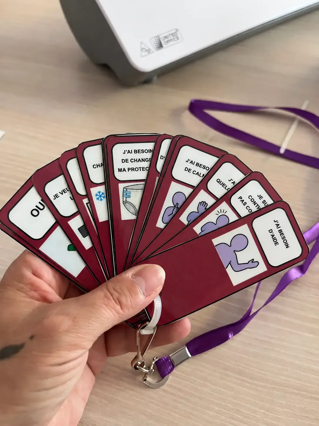 Cartes de CAA en français avec illustrations et textes relatifs à la santé et à la sécurité, une main les tient en éventail pour montrer un dispositif de CAA personnalisé.