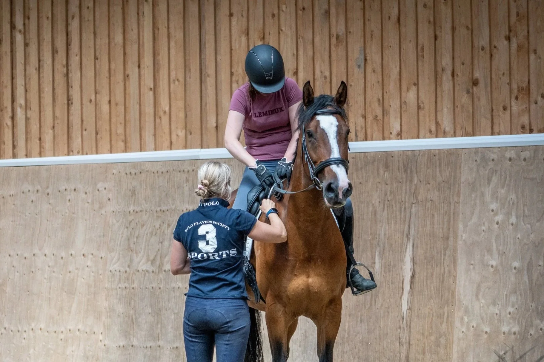 Christina Wiederkehr coaching a local rider with her show-jumping ability in the indoor arena.