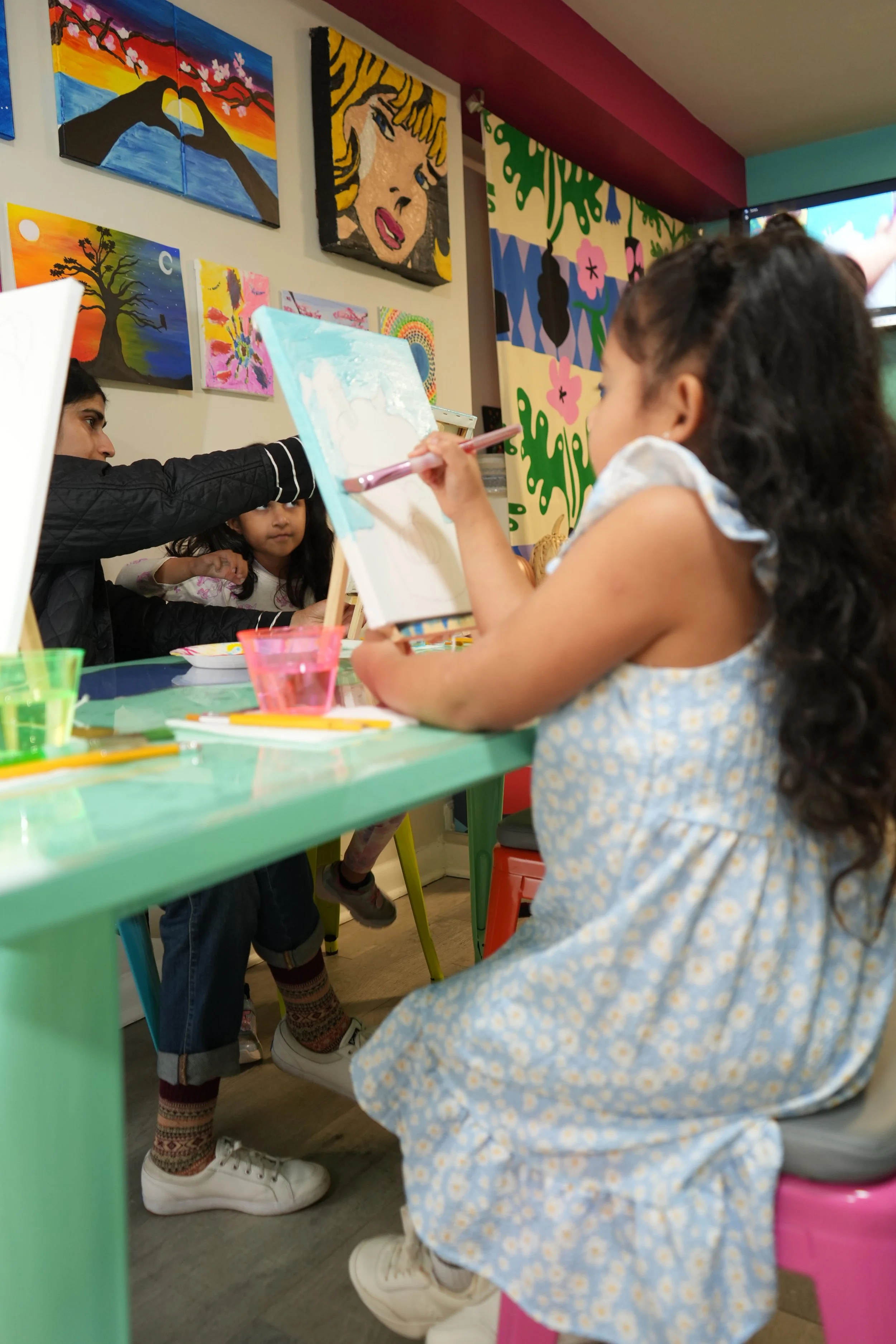 Children painting in an art studio with colorful artwork on the walls.