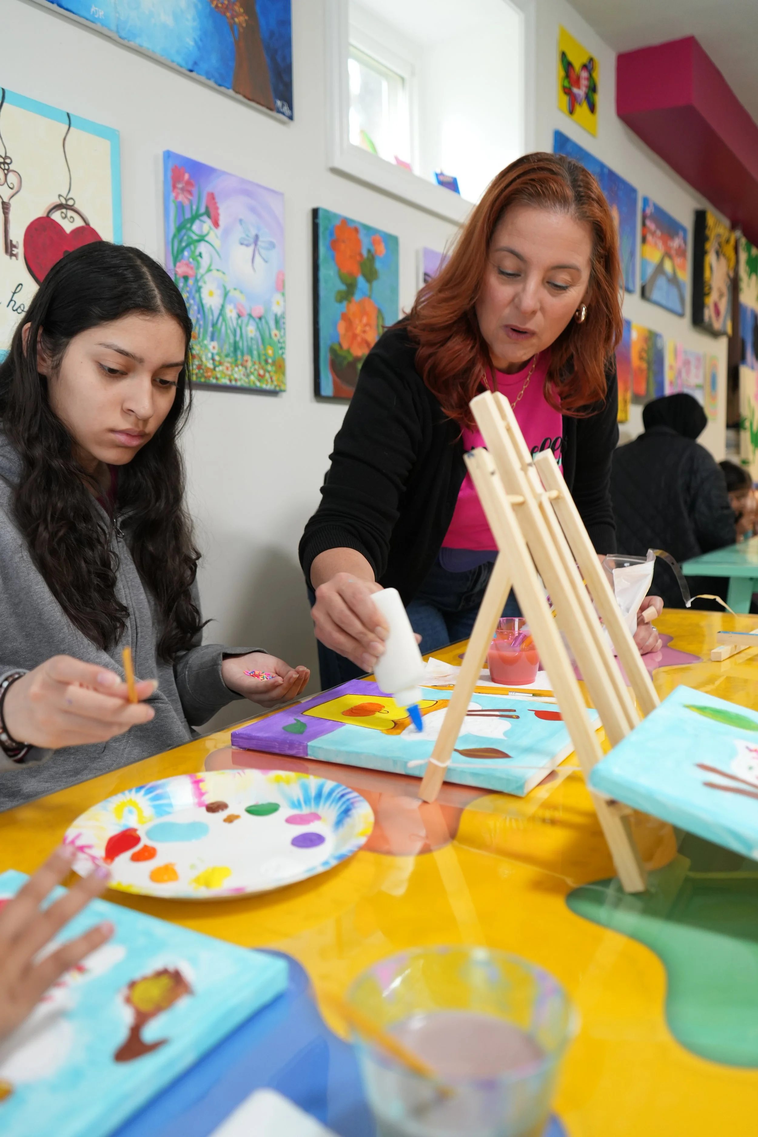 People engaging in a painting activity at a colorful art class, with various paintings hanging on the wall.