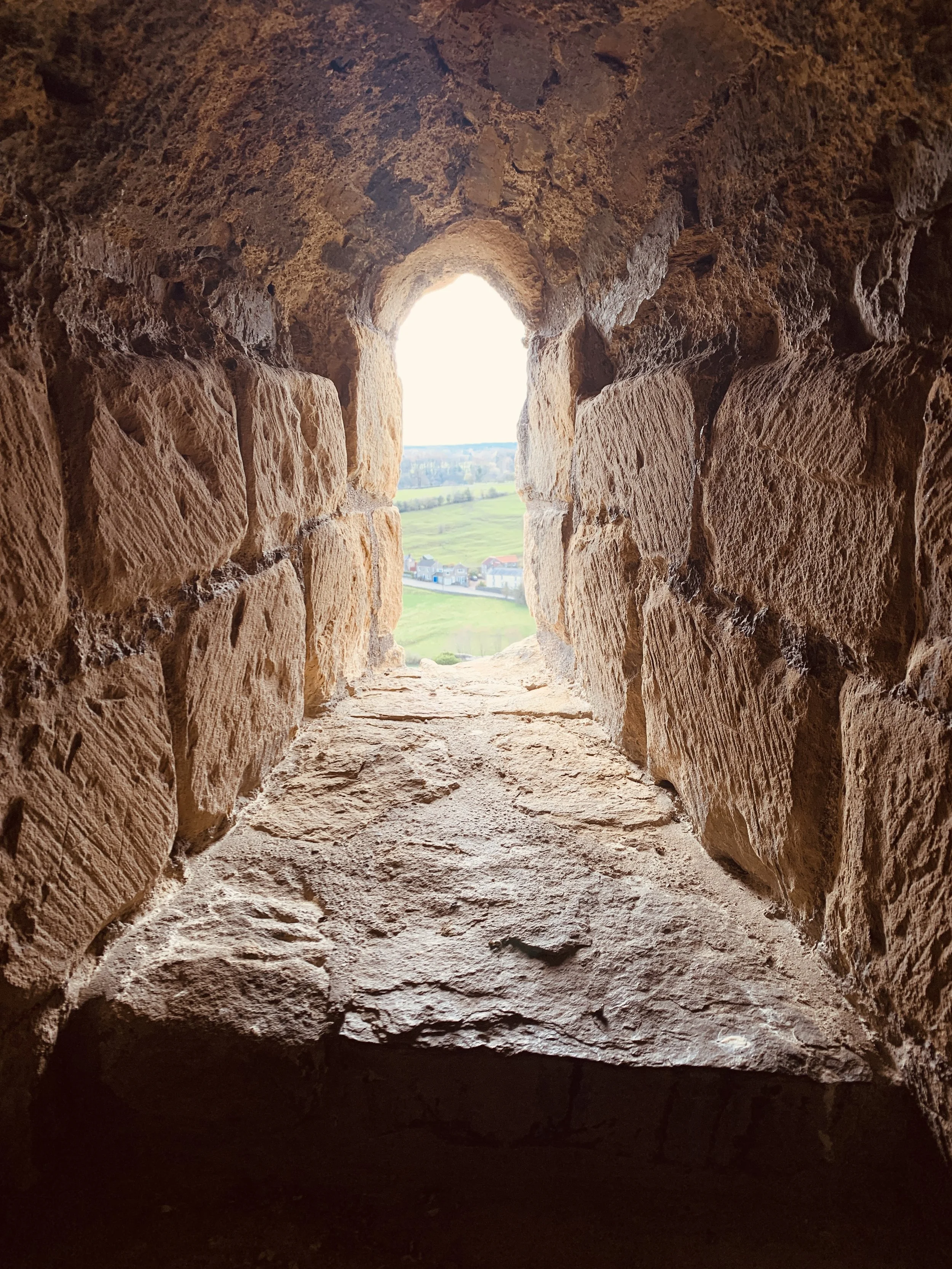 View from inside an ancient stone window looking out over green fields and a small village.