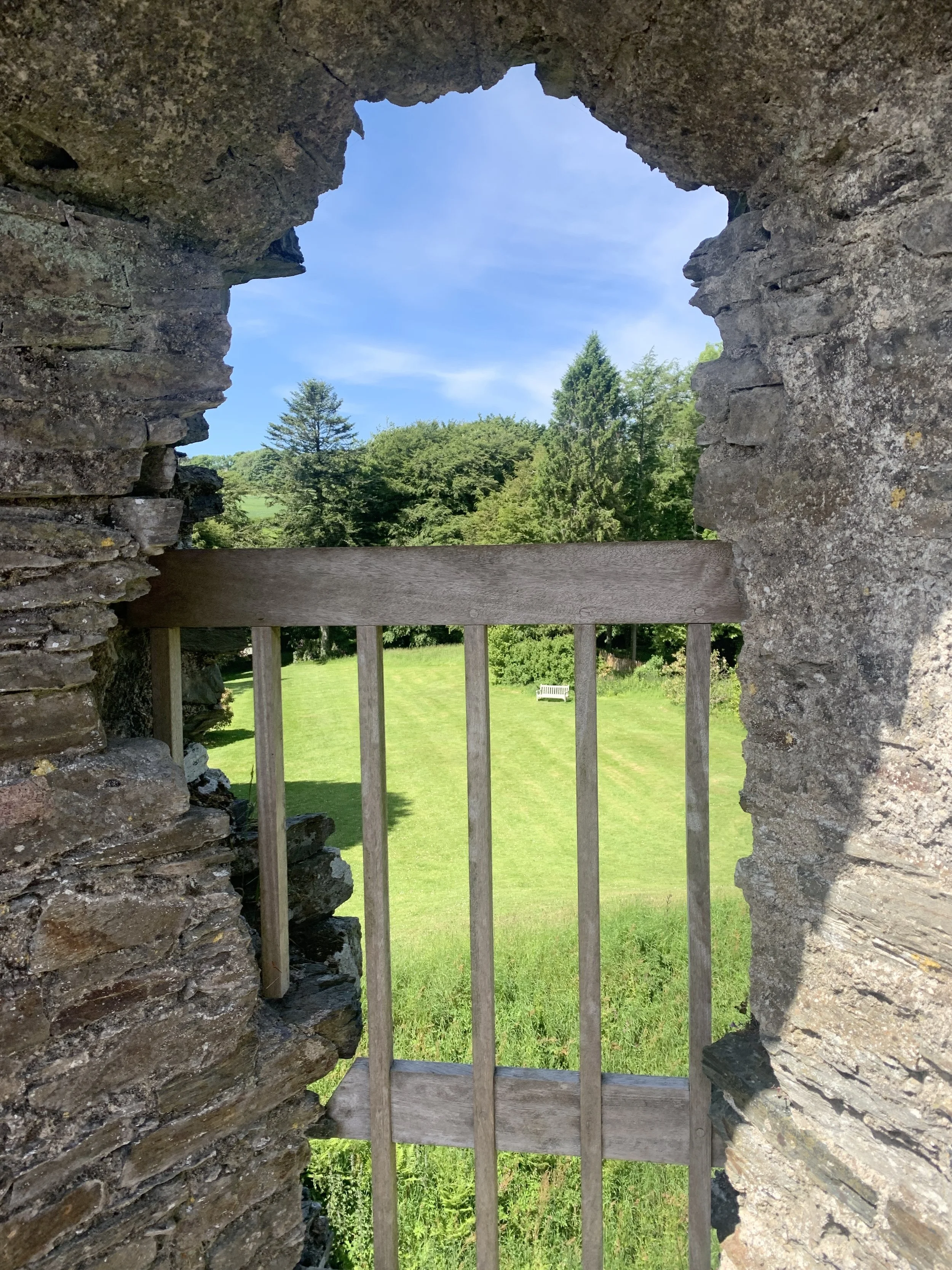Stone window frame with a view of a grassy area, trees, and a blue sky with some clouds.