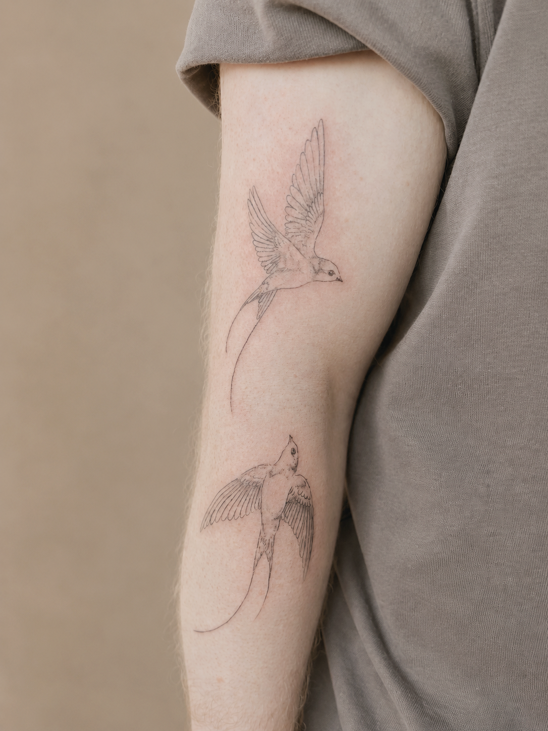 A tattoo of two swallow birds in flight on a person's upper arm, outlined in black ink.