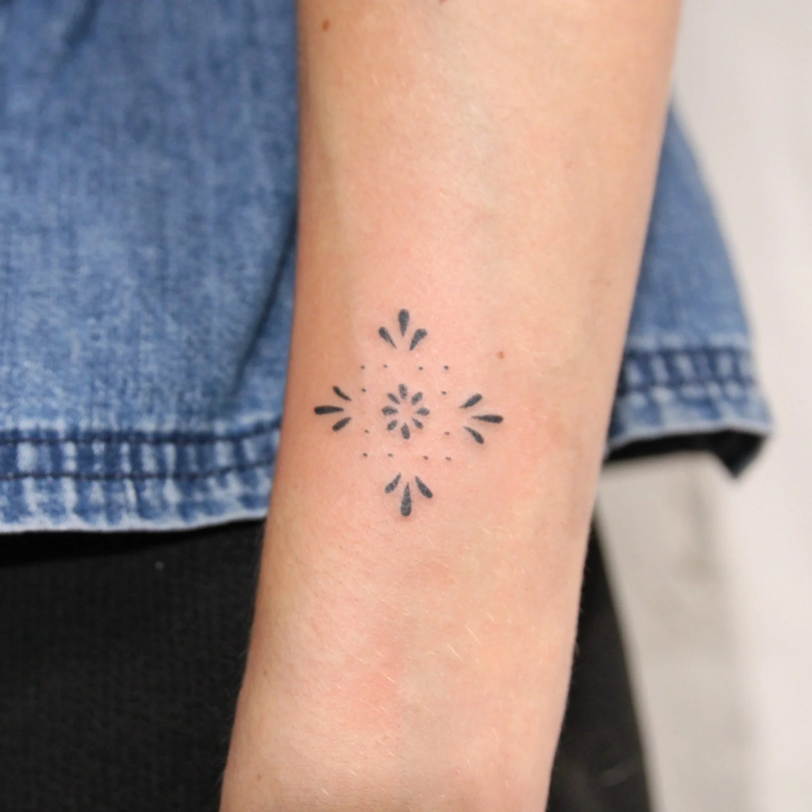 Close-up of a person's arm with a small black tattoo of a geometric floral pattern.