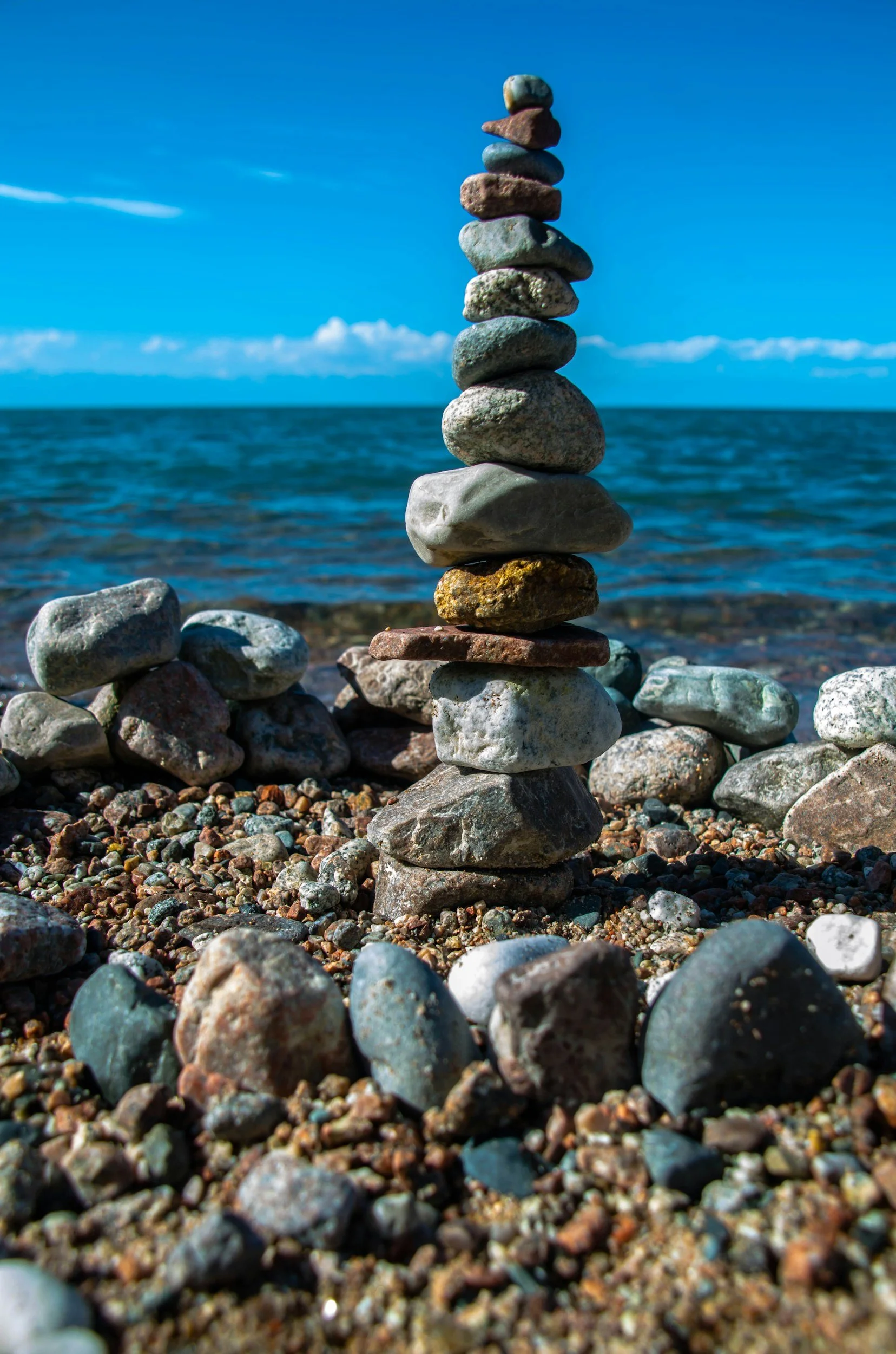 A stack of balanced stones on a rocky beach by the ocean with a blue sky and some clouds in the background.