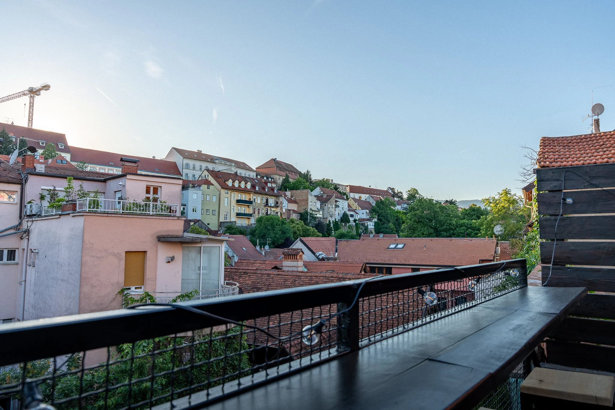 Cityscape view from a balcony with rooftops and colorful buildings, under a clear blue sky.