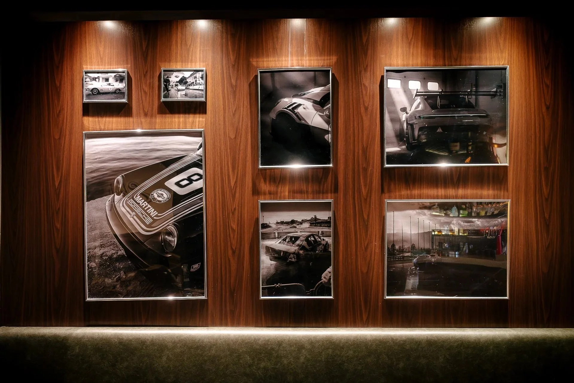 A wooden wall with framed vintage black and white car photographs on display, illuminated by ceiling lights.