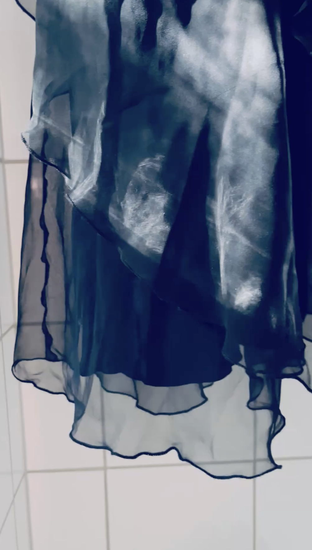 A sheer black fabric of a dress hanging against white tiled bathroom wall.