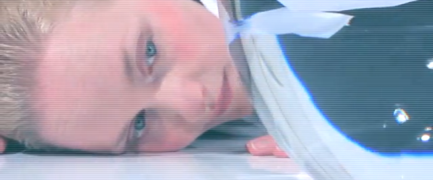 A person with blond hair lying face down on a flat surface, looking directly at a glass bowl.