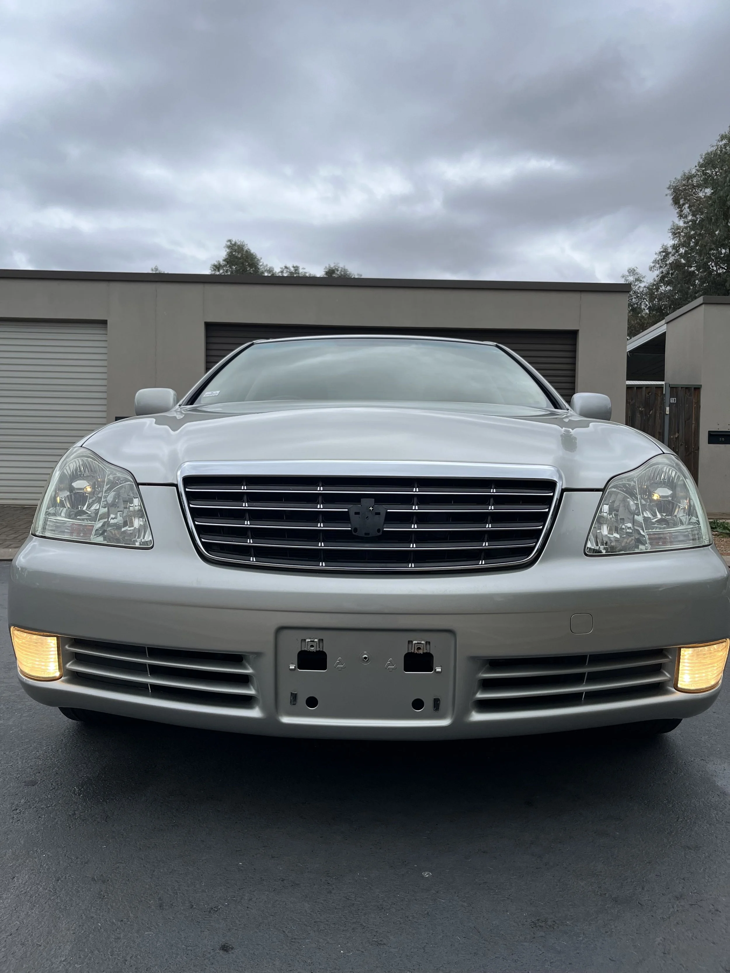 Front view of a silver car parked on asphalt with a gray building and cloudy sky in the background