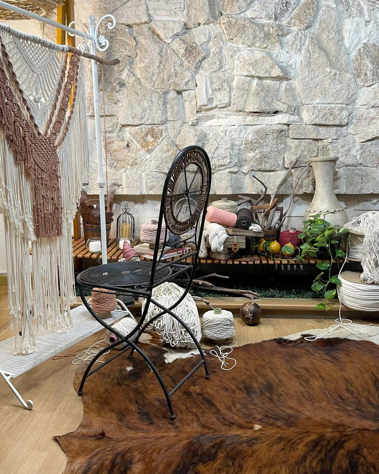 A cozy indoor space with a rustic stone wall, various decorative items, plants, yarn, and a cowhide rug.