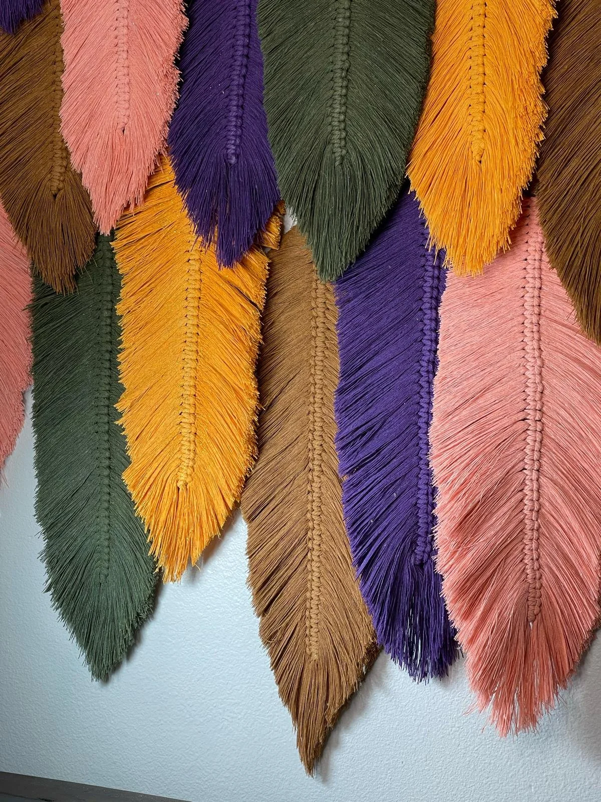 Colorful dried palm leaves in pink, purple, green, orange, and brown hanging on a wall.