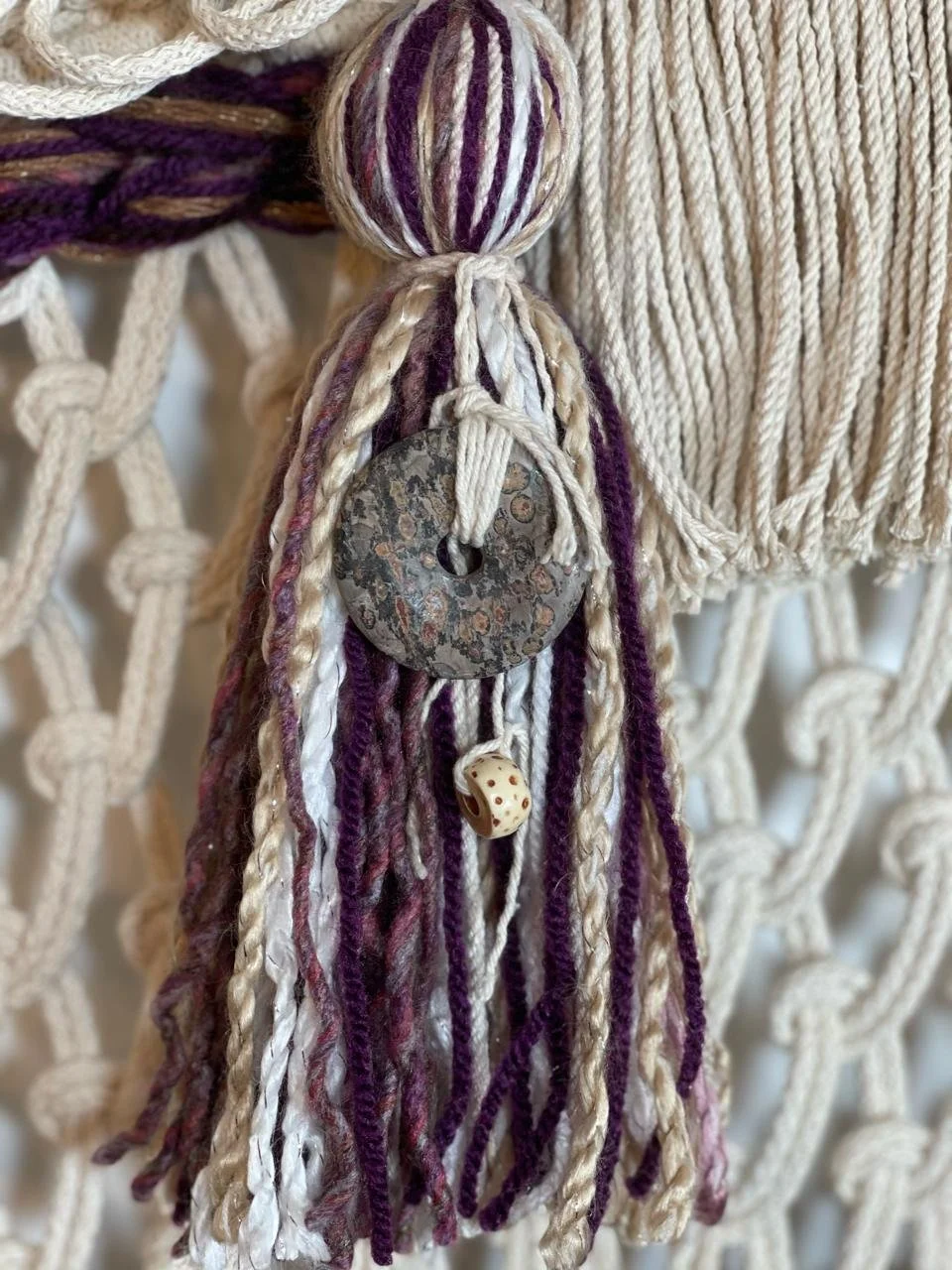 Close-up of decorative tassels made from multicolored yarn and two small beads, hanging against a textured woven background.