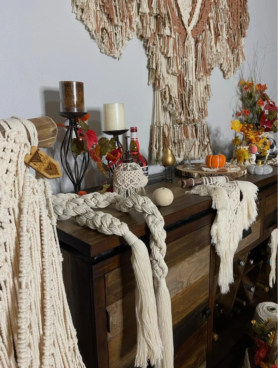 Decorative table with candles, pumpkins, flowers, and macramé wall hangings in a cozy room.