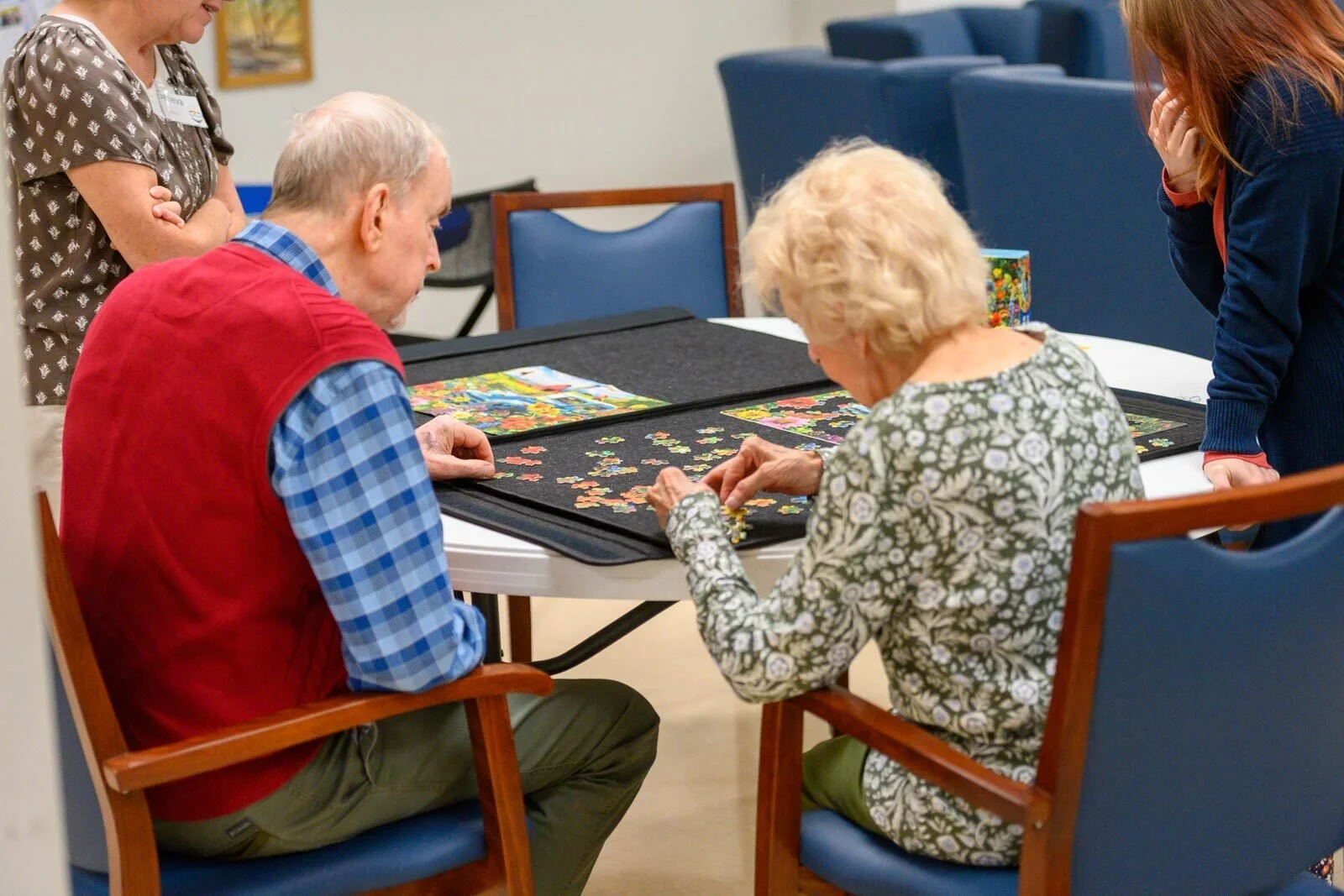 Two elderly women and two middle-aged women around a table working on a jigsaw puzzle together.