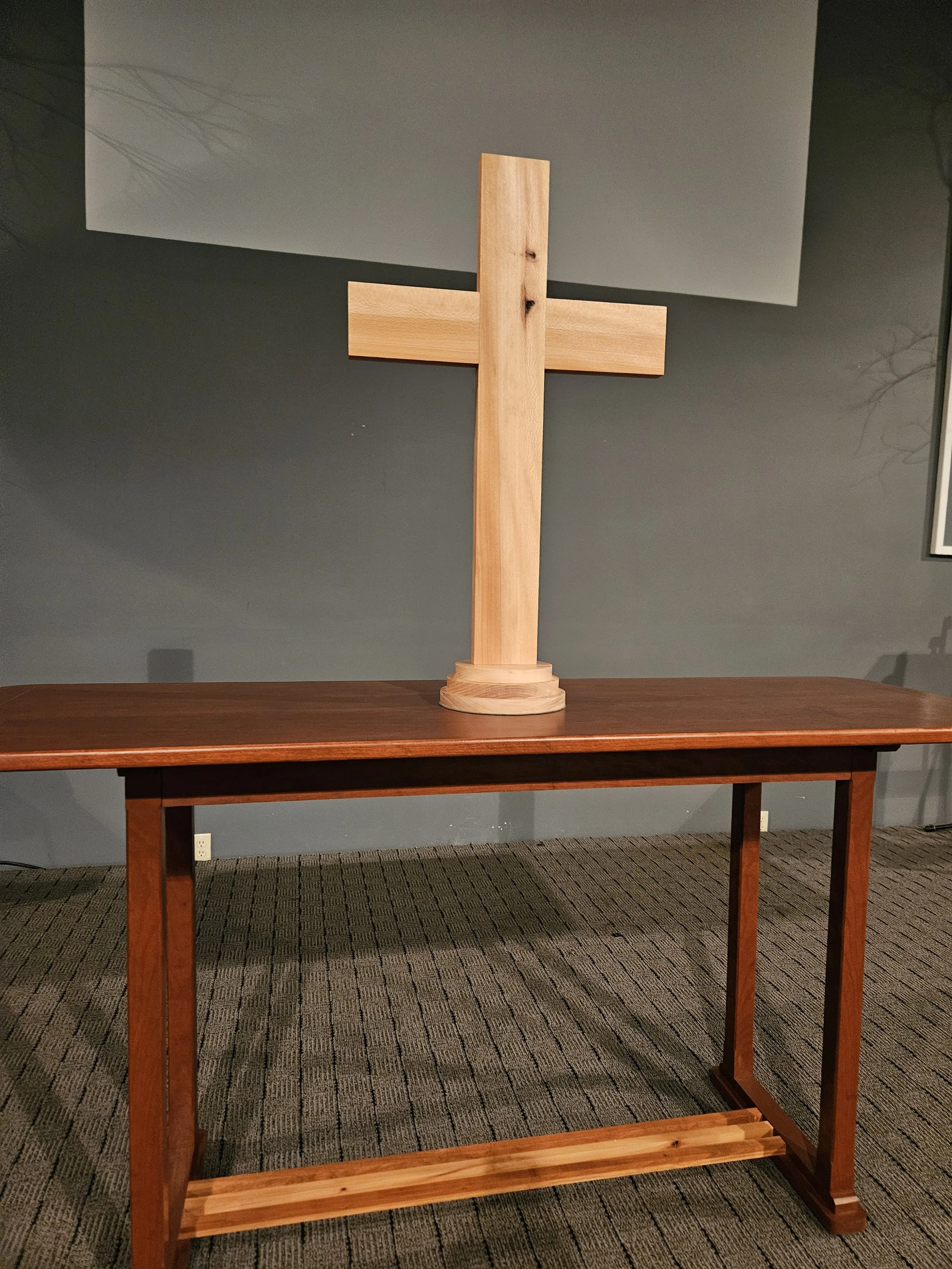 A wooden cross on a table against a dark gray wall.