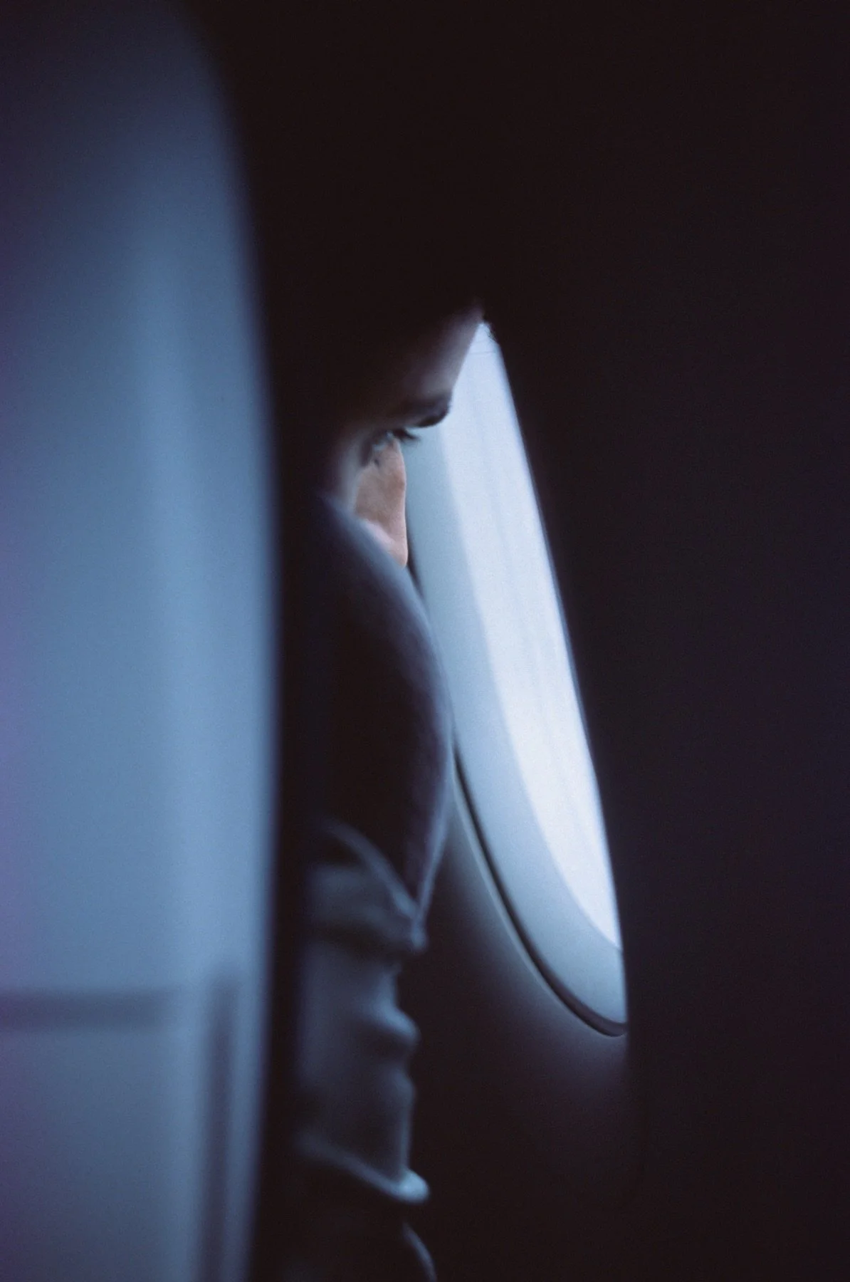Close-up of a person looking out of an airplane window, with headphones on, in a dark environment.