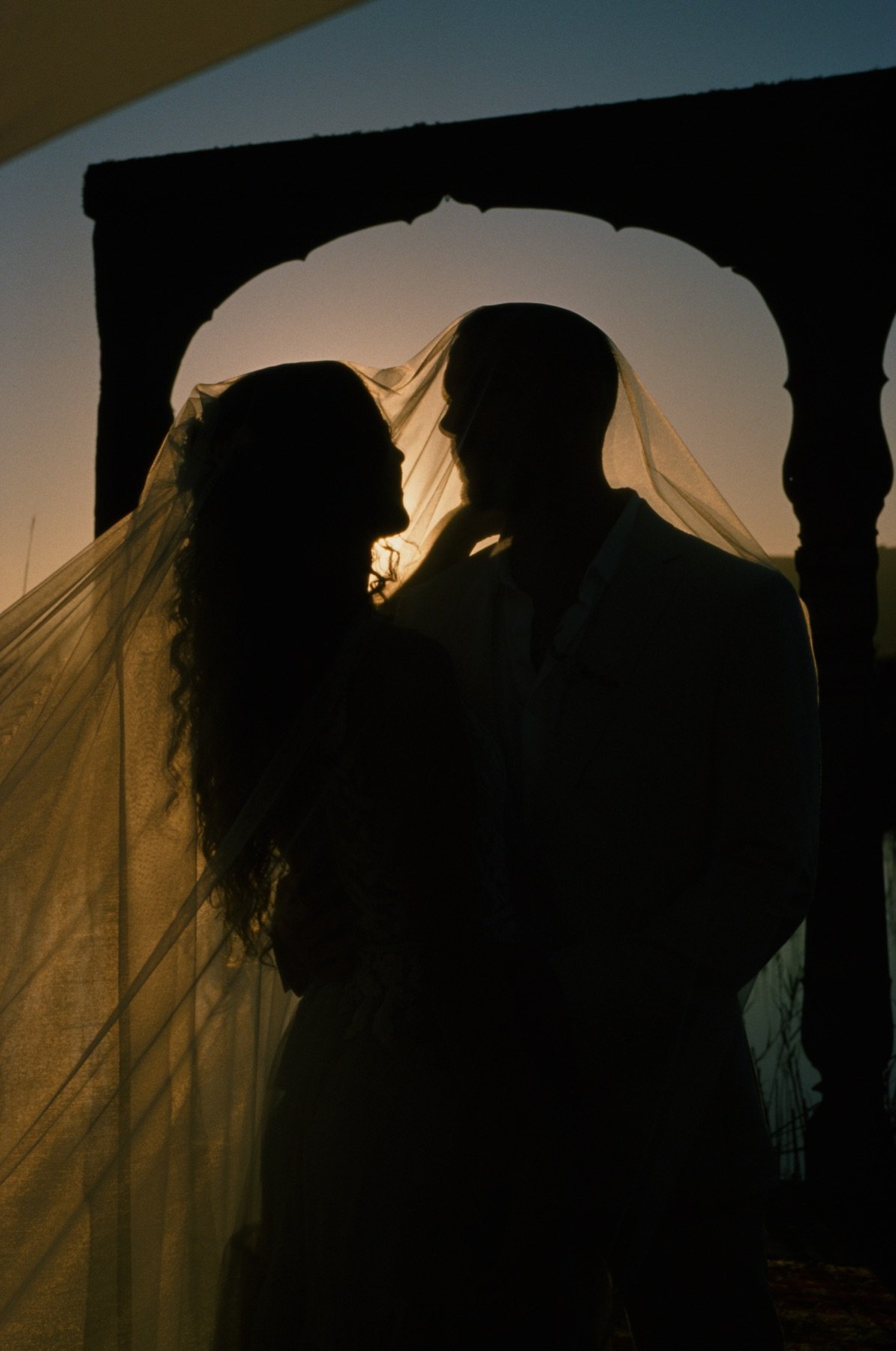 Silhouette of a couple under a veil with sunset in the background.