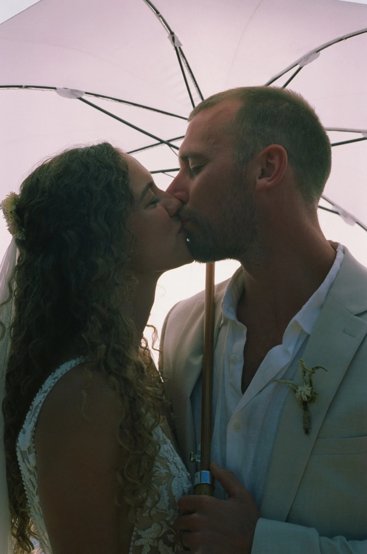A bride and groom share a kiss under an umbrella during their wedding ceremony.