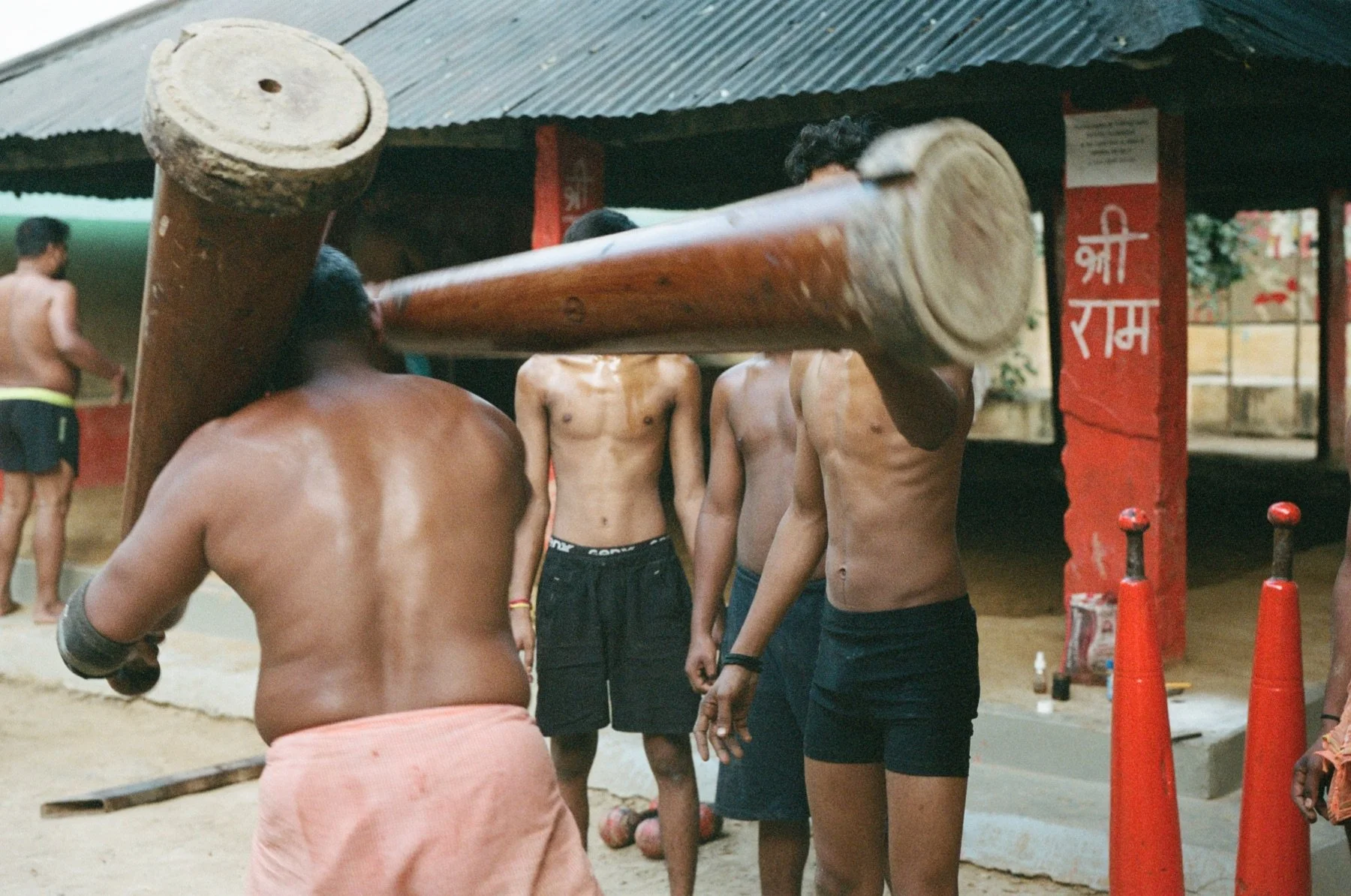 Group of men practicing or participating in a traditional Indian sport called Dahi Handi, with some shirtless men lifting a large wooden pot on a pole.