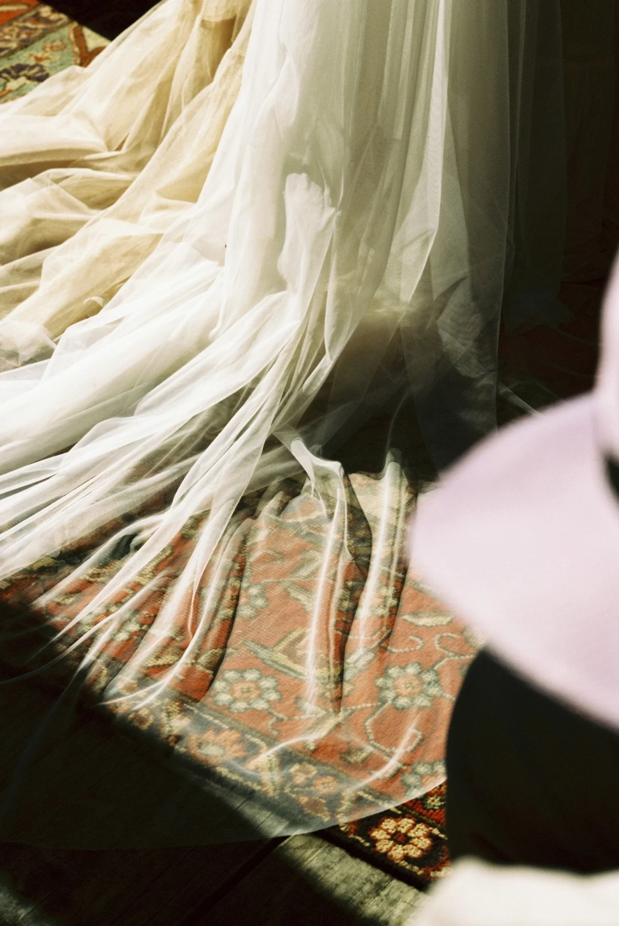Multiple layers of sheer curtain fabric draped over a patterned carpet, with part of a black object visible on the right side.