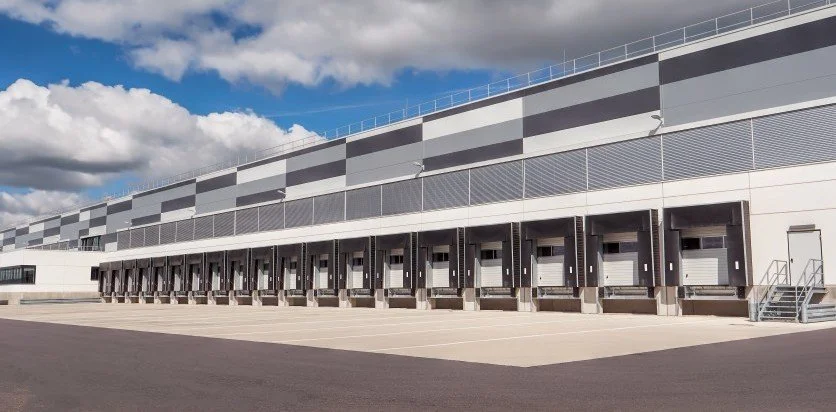 Exterior of a large warehouse or distribution center with multiple loading docks and a paved parking area