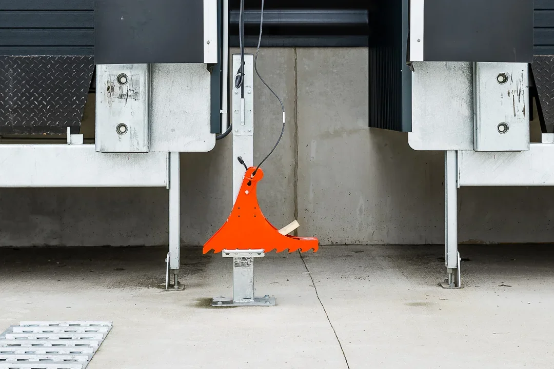 Orange safety hook attached to a metal support, positioned between industrial equipment on a concrete floor.