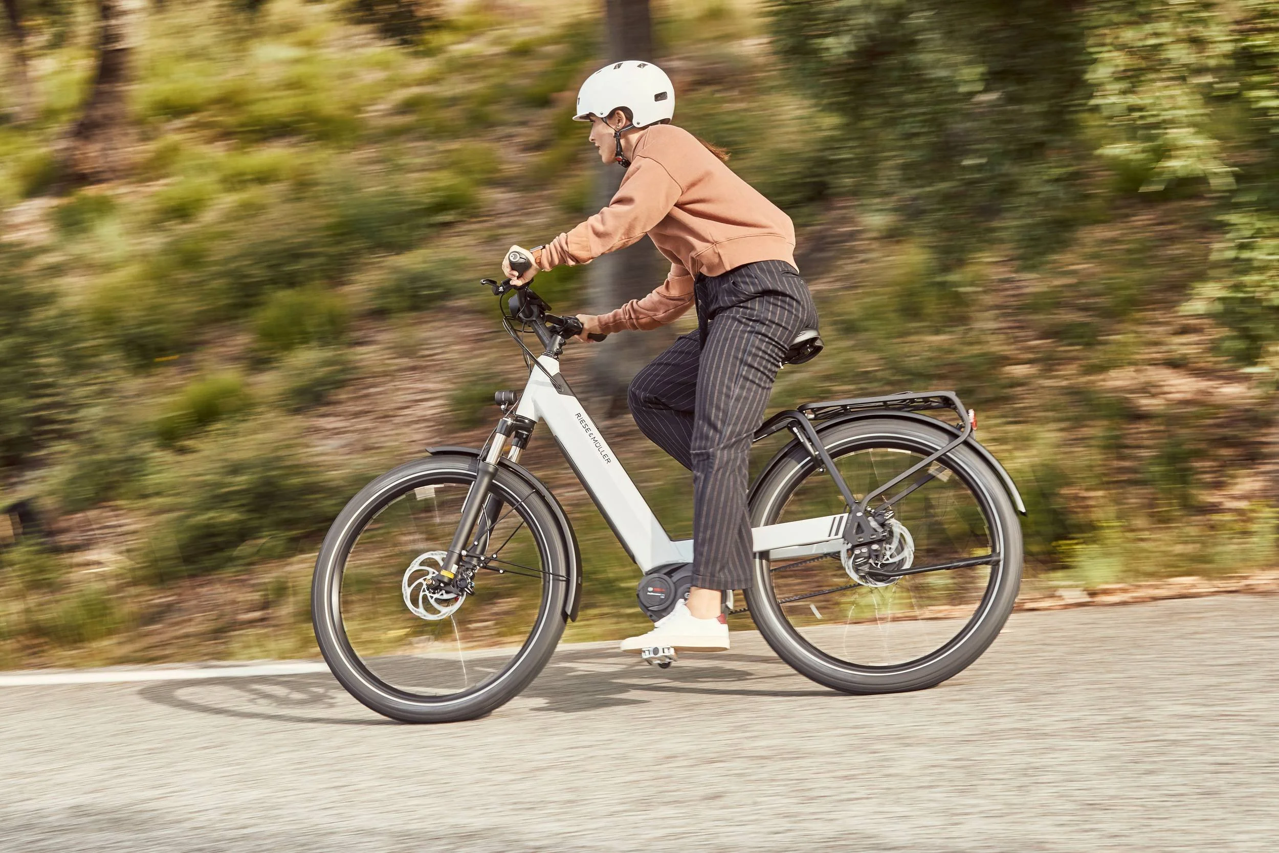 Frau fährt weisses E-Bike, Hintergrund in Bewegungsunschärfe